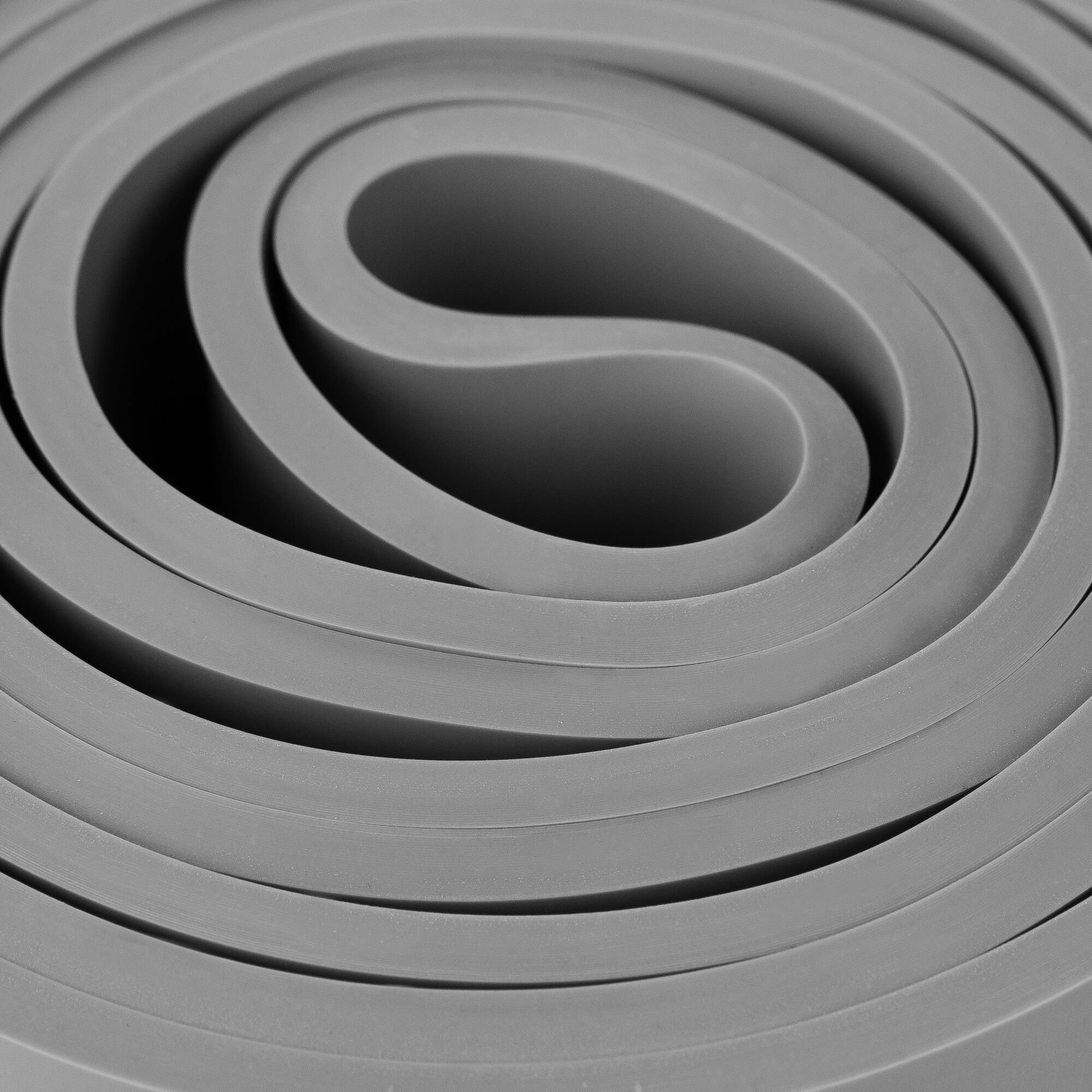 Zbliżenie zwiniętego, szarego materiału gumowego. Warstwy tworzą spiralny wzór. Tło to cień.