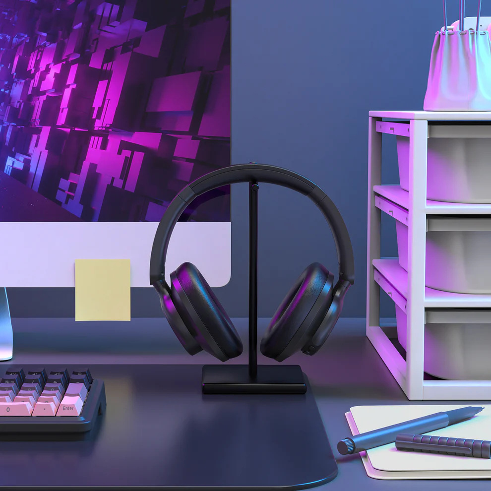 Słuchawki na stojaku, komputer z różowo-fioletowym wyświetlaczem, klawiatura, notatnik, długopis i półka z pojemnikami.