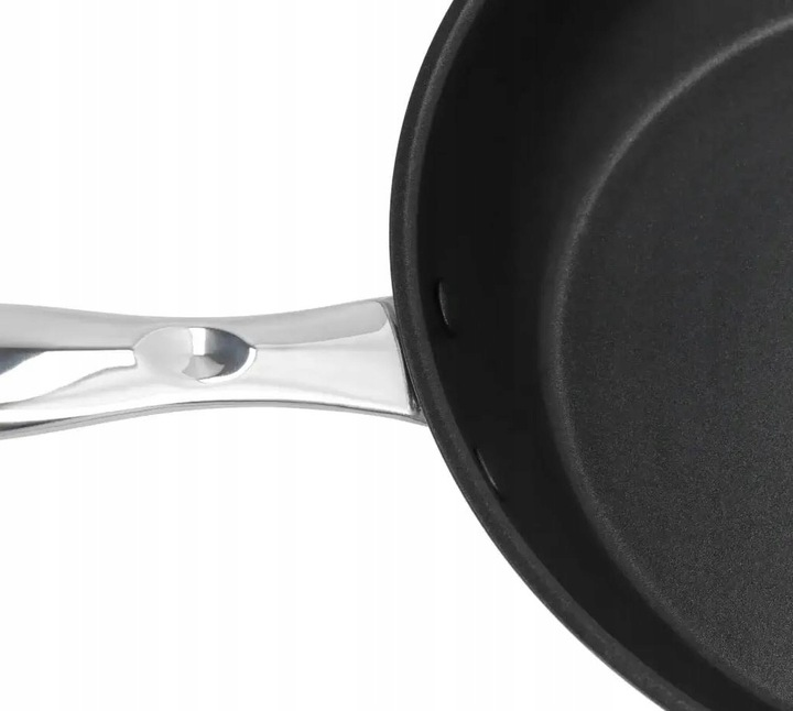 Zbliżenie czarnej patelni ze srebrnym uchwytem. Patelnia jest okrągła, a uchwyt zakrzywiony. Białe tło.