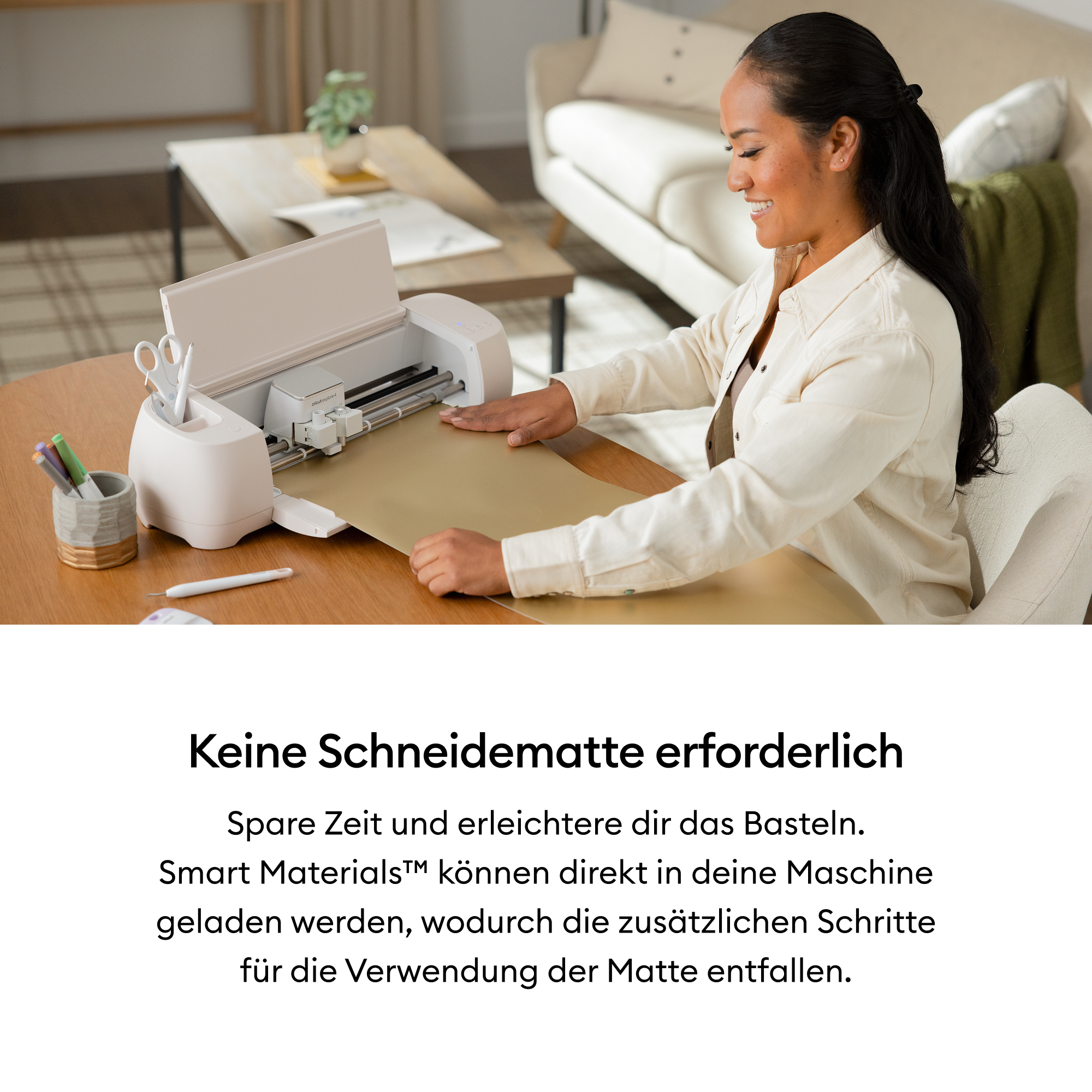 Eine Frau lächelt, während sie eine weiße Schneidemaschine auf einem Holztisch benutzt. Schere und Stifte sind in einem Halter.