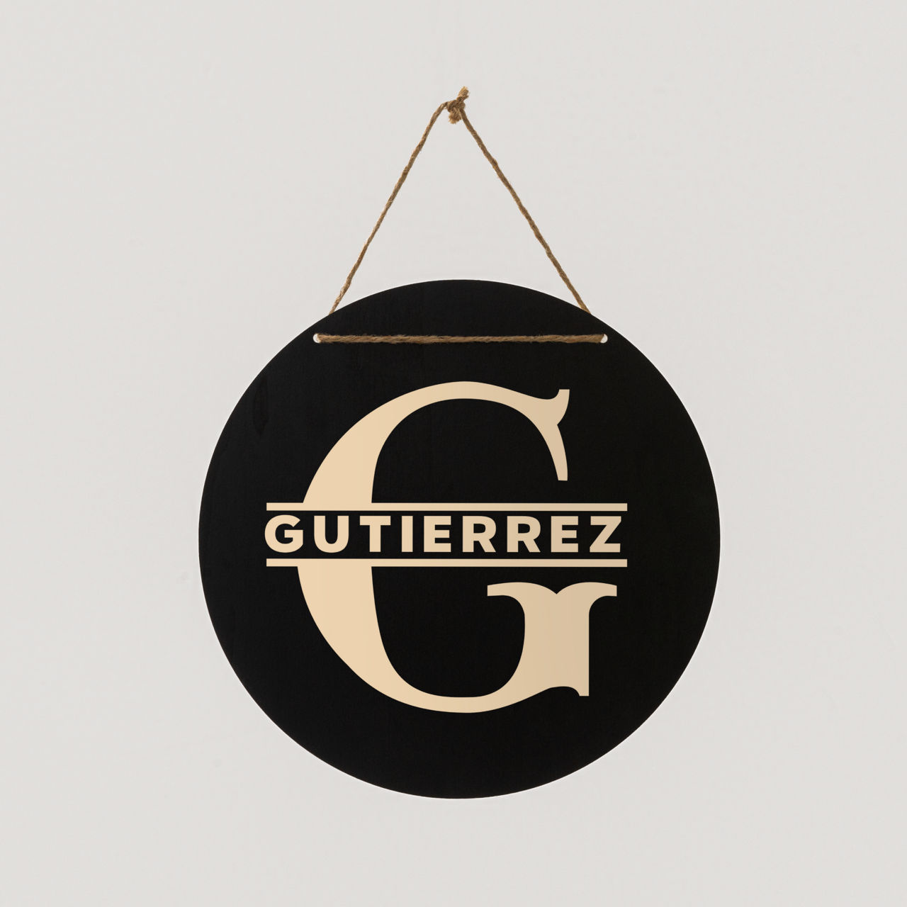 Ein rundes schwarzes Schild mit einem goldenen 'G' und dem Namen 'Gutierrez'. Es hängt an einer Schnur vor weißem Hintergrund.