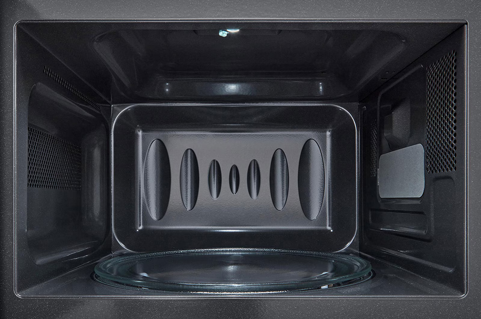 Wnętrze ciemnej kuchenki mikrofalowej. Szklana płyta na dole. Wnętrze ma owalne otwory wentylacyjne i światło na górze.