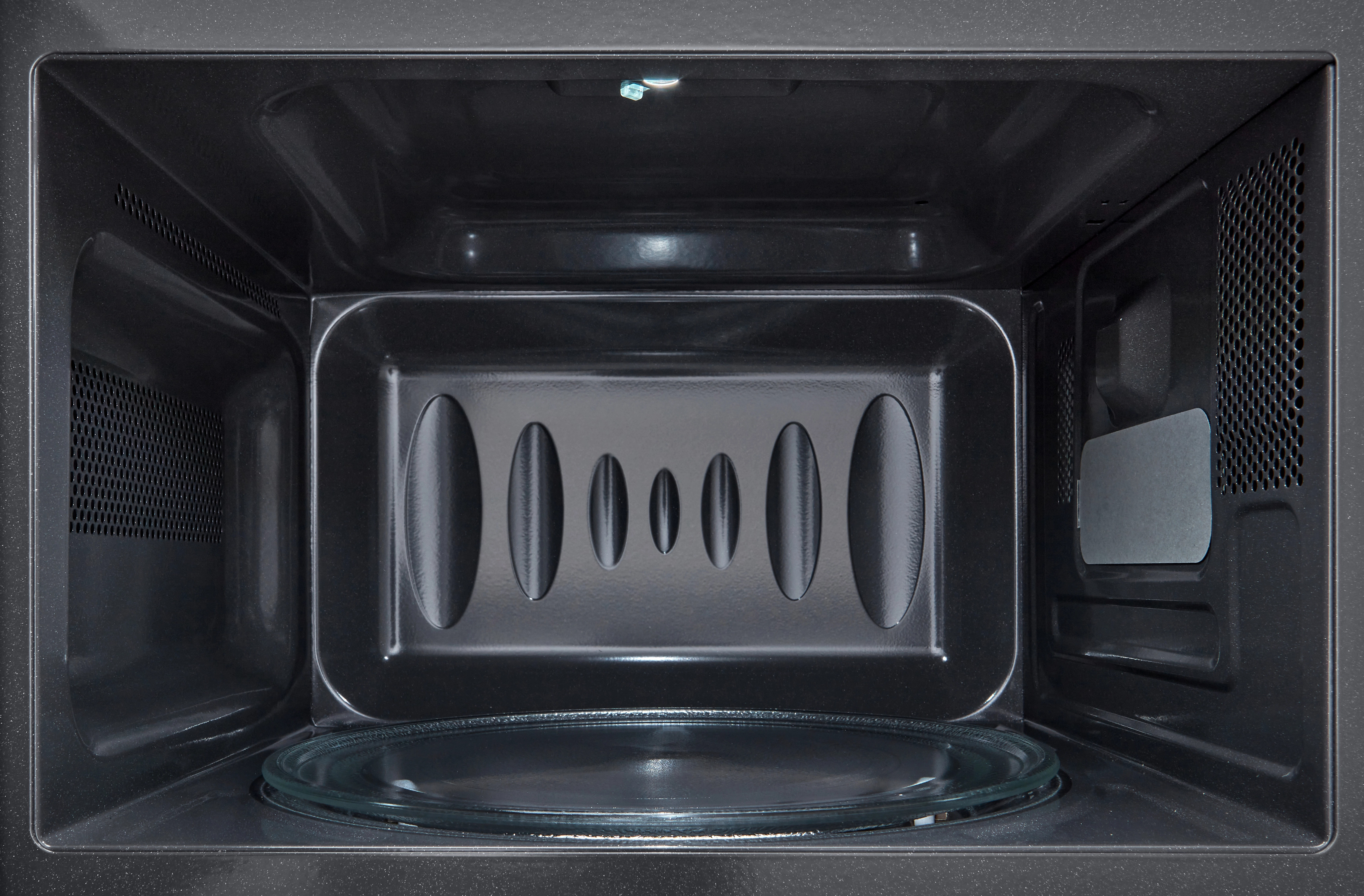 Wnętrze czarnej kuchenki mikrofalowej. Szklany talerz na dole. Wnętrze ma owalne otwory wentylacyjne i światło.