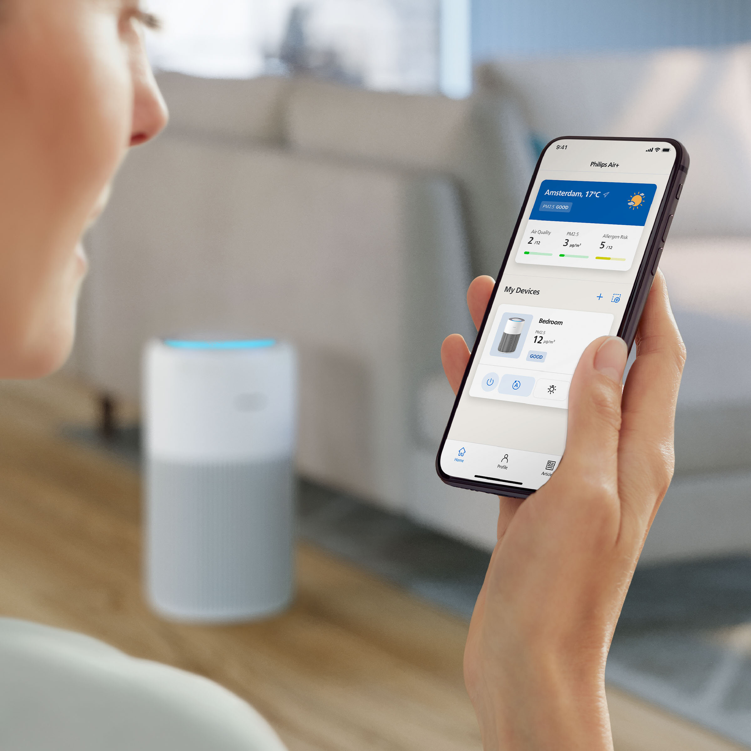 Osoba trzyma telefon z danymi o jakości powietrza. Oczyszczacz powietrza jest w tle.