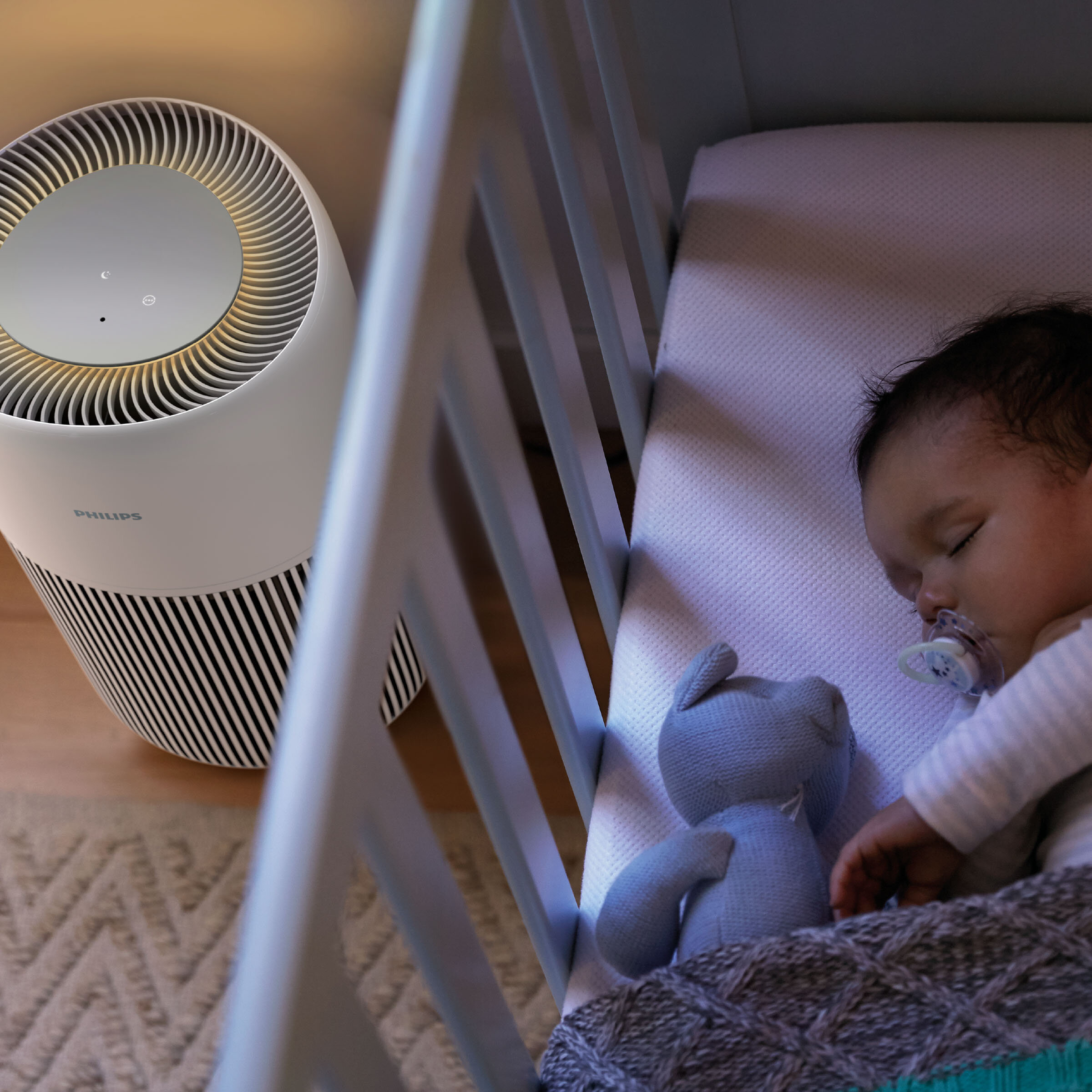 Śpiące dziecko w łóżeczku z pluszakiem i oczyszczaczem powietrza Philips.