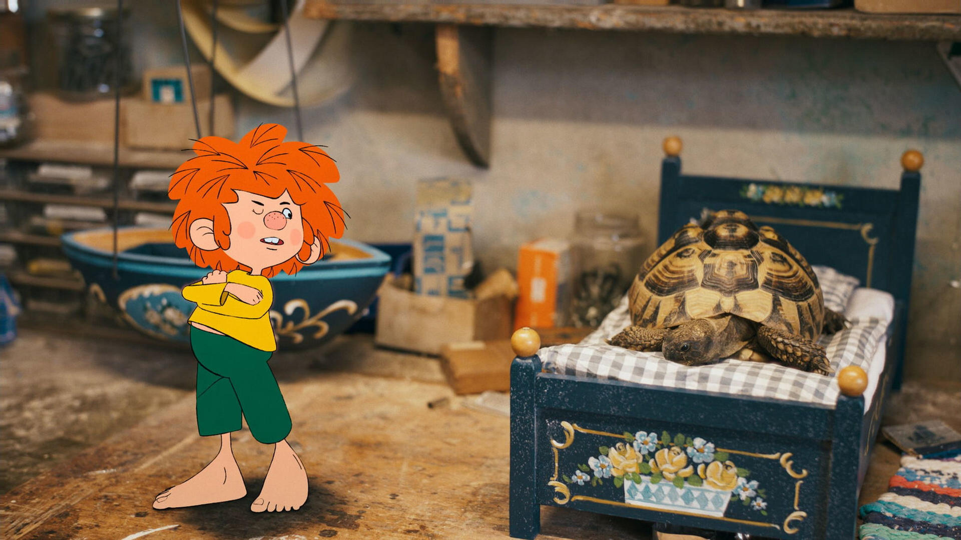 Ein Cartoon-Junge mit roten Haaren und verschränkten Armen blickt auf eine Schildkröte in einem Bett. Die Szene ist in einer Werkstatt.