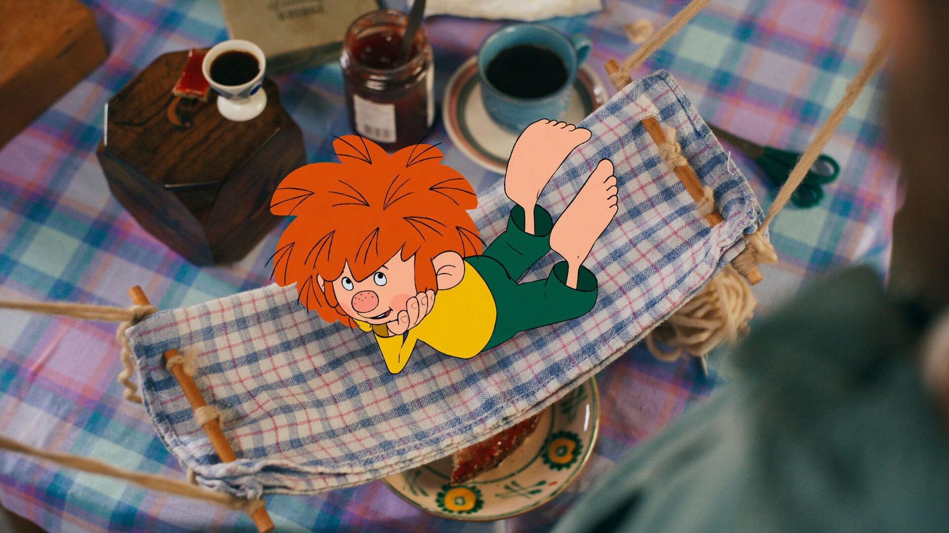 Ein Cartoon-Kind mit orangefarbenem Haar entspannt sich in einer kleinen Hängematte. Im Hintergrund ein Tisch mit Essen und Getränken.