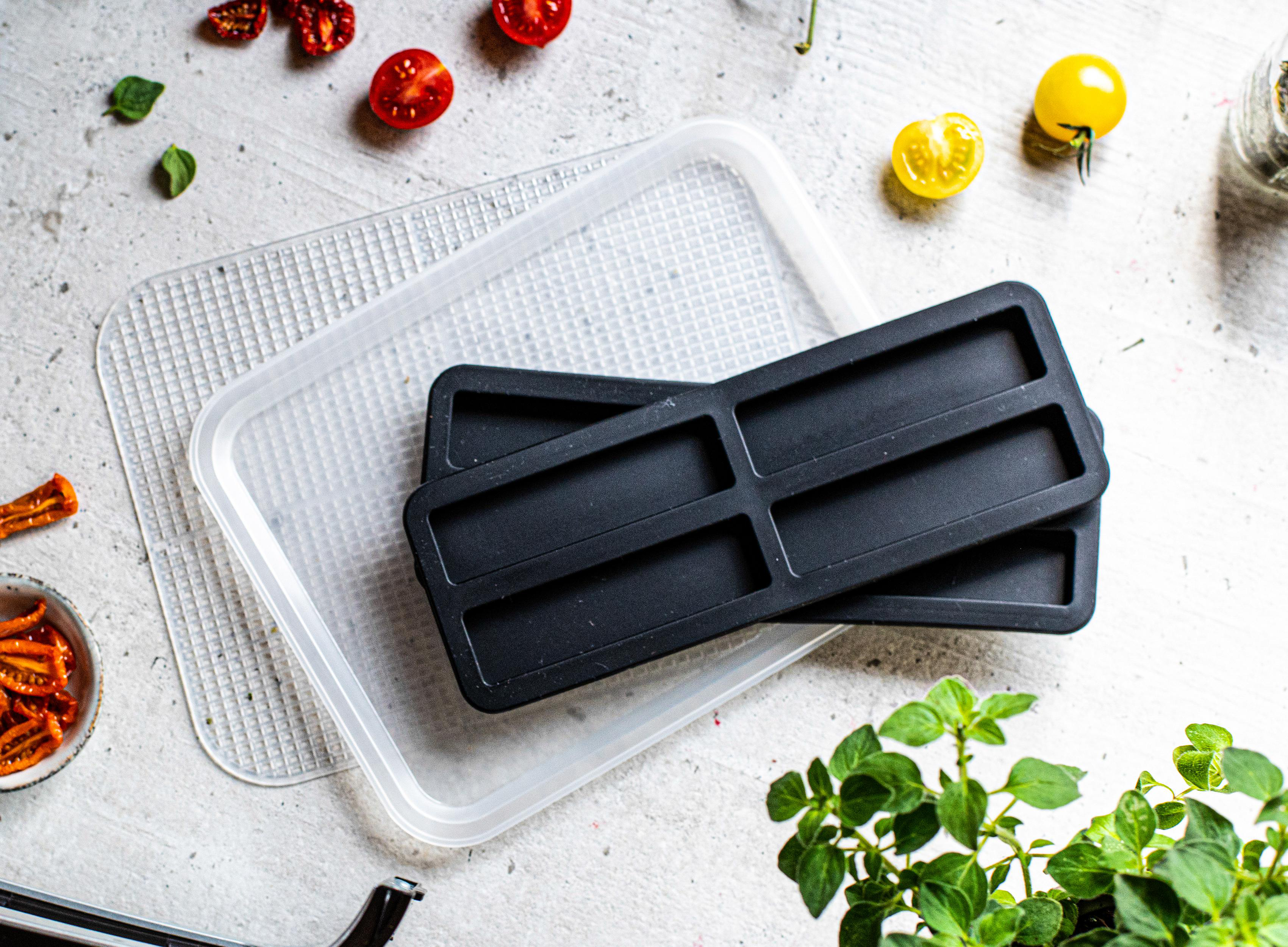 Draufsicht auf die Essenszubereitung. Enthält schwarze Formen, Tomaten, Kräuter und einen transparenten Behälter.