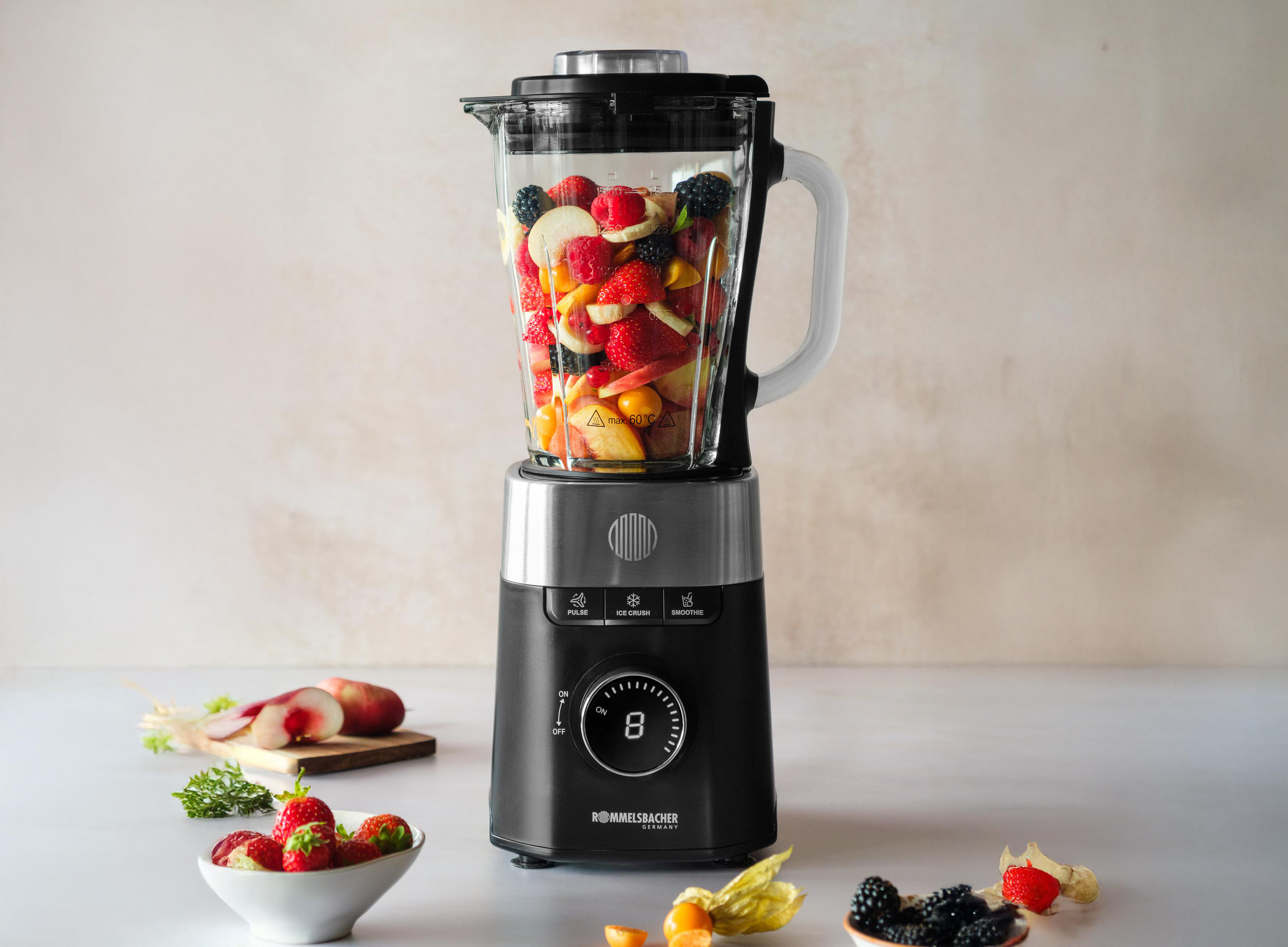 Mixer gefüllt mit Früchten, Beeren. Erdbeeren in einer Schüssel, Pfirsichstücke, Brombeeren und Andenbeeren.