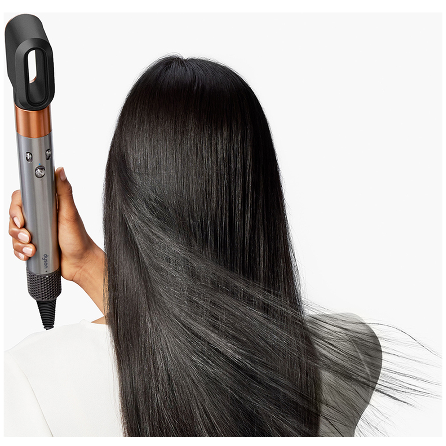 Een persoon houdt een Dyson-föhn vast en stylet lang, steil zwart haar tegen een witte achtergrond.