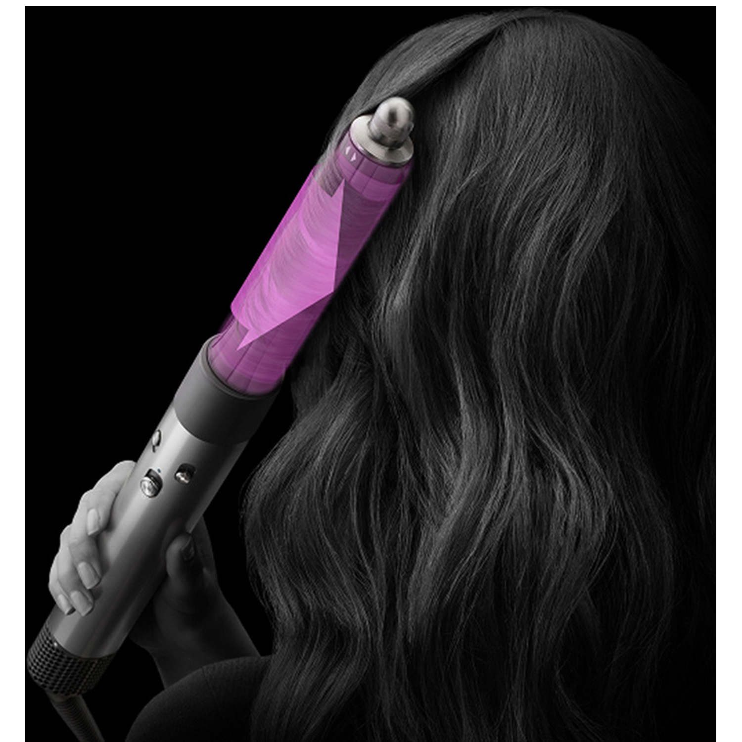 Een persoon houdt een zilveren haarstylingtool vast met een paarse cilinder. De tool bevindt zich in de buurt van het zwarte haar van de persoon tegen een zwarte achtergrond.