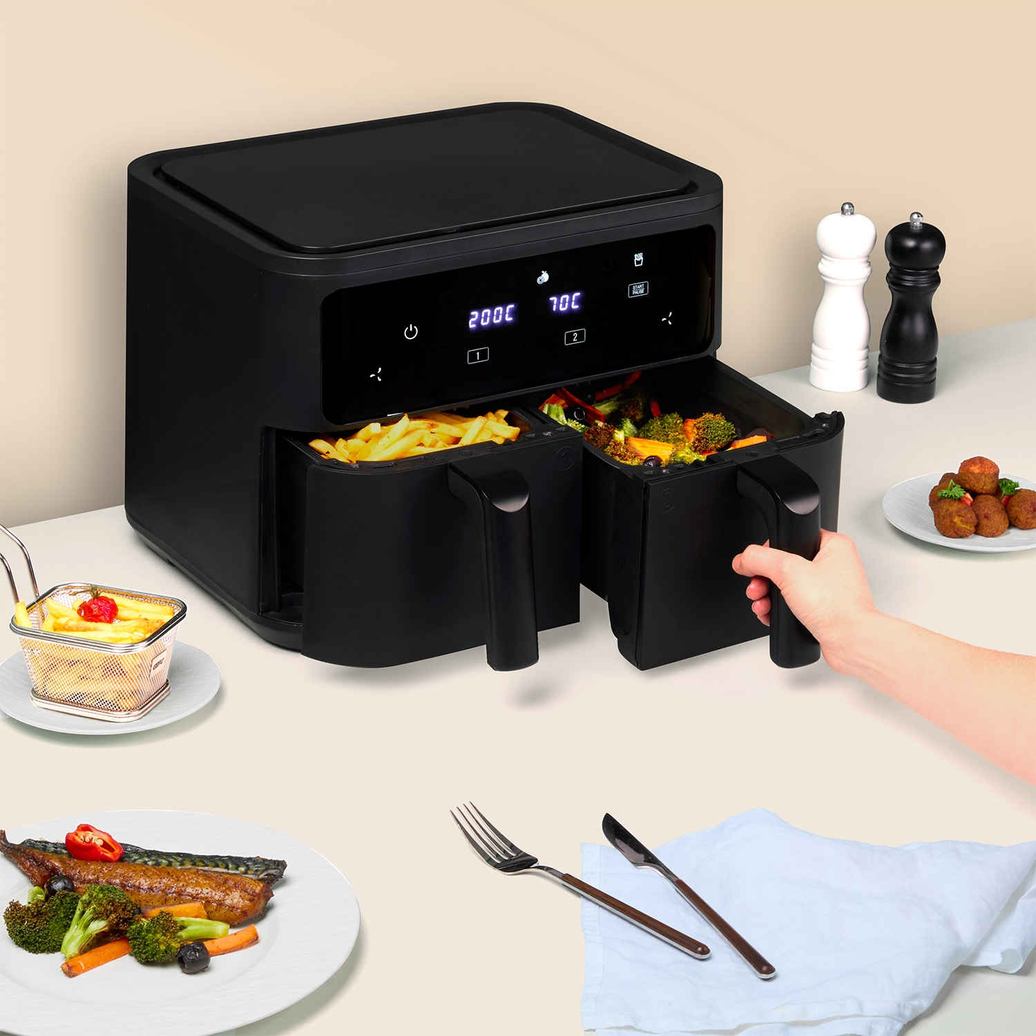 Friggitrice ad aria nera con cibo nei cassetti, mano che ne tiene uno. Patatine fritte, verdure e pesce cotto su piatti. Saliere e pepiere.