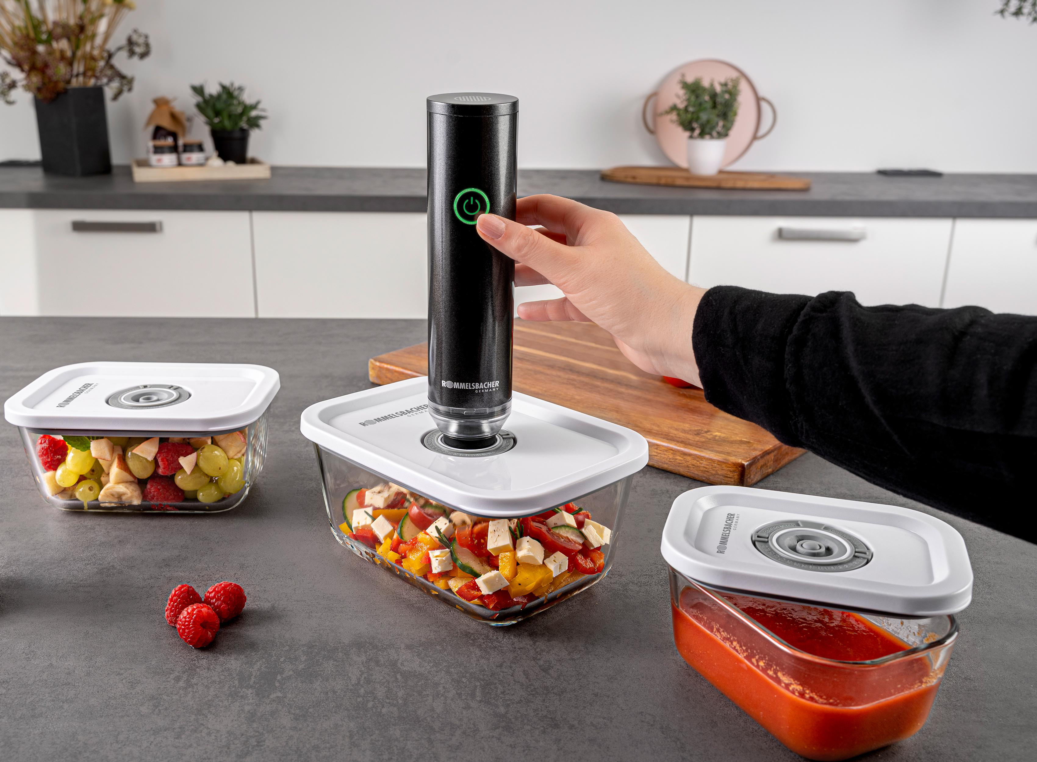Eine Person verwendet einen Vakuumierer auf einem Lebensmittelbehälter. Es gibt weitere Behälter mit Essen auf einer grauen Arbeitsplatte.