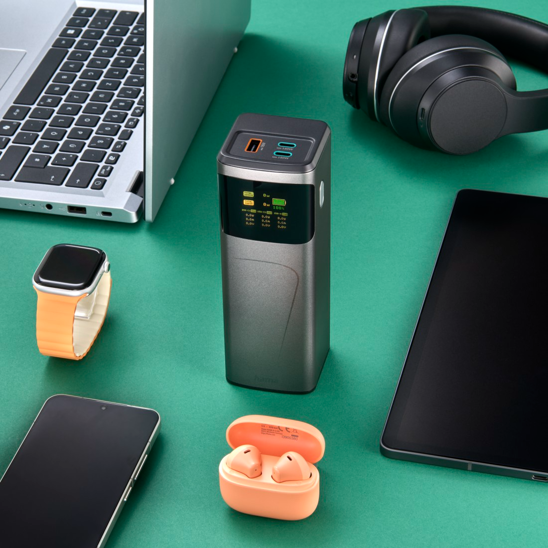 Egy power bank, laptop, fejhallgató, tablet, óra, telefon és fülhallgató zöld felületen.
