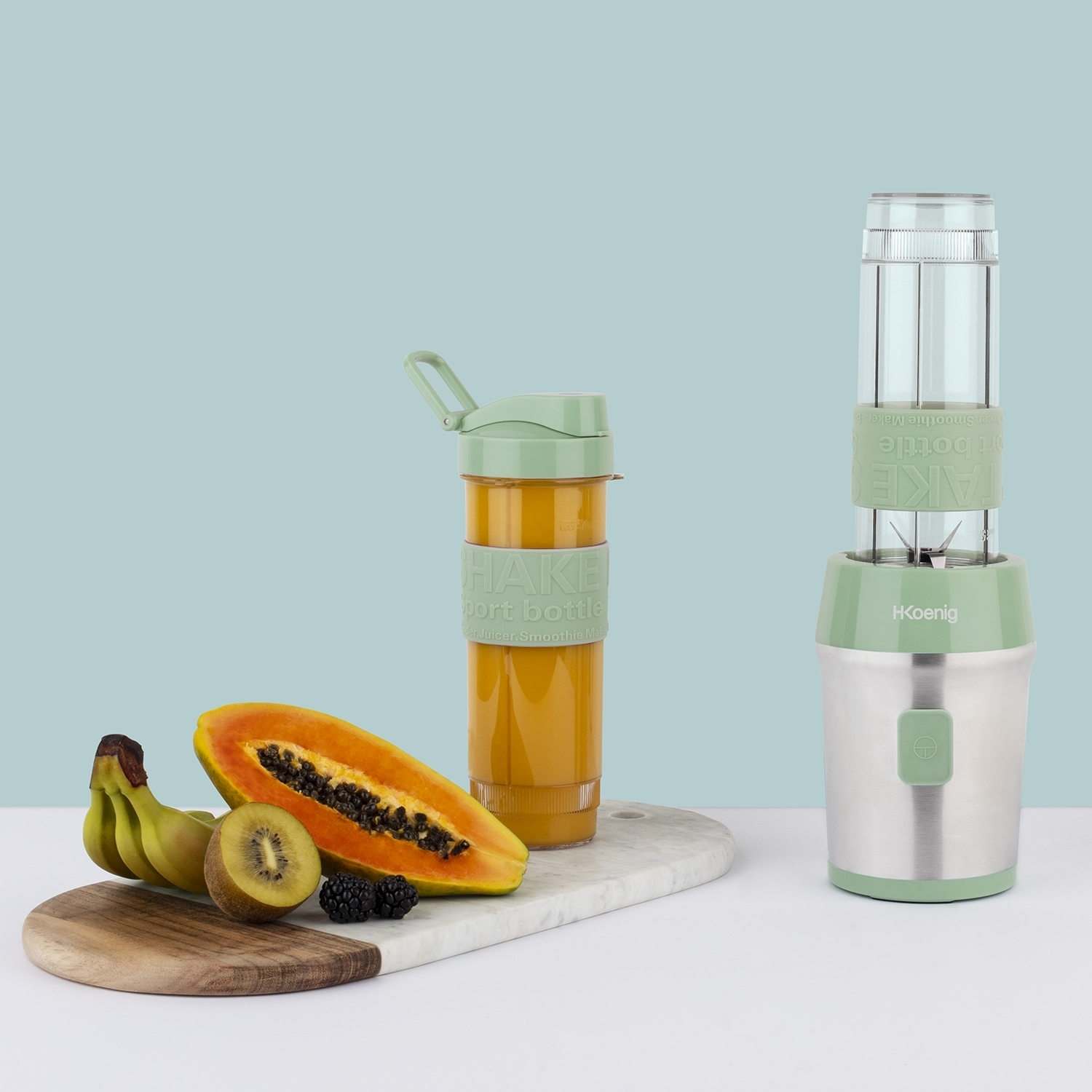 Un frullatore e una bottiglia di frullato sono accanto a frutta: papaya, kiwi, banane e more. Lo sfondo è azzurro.