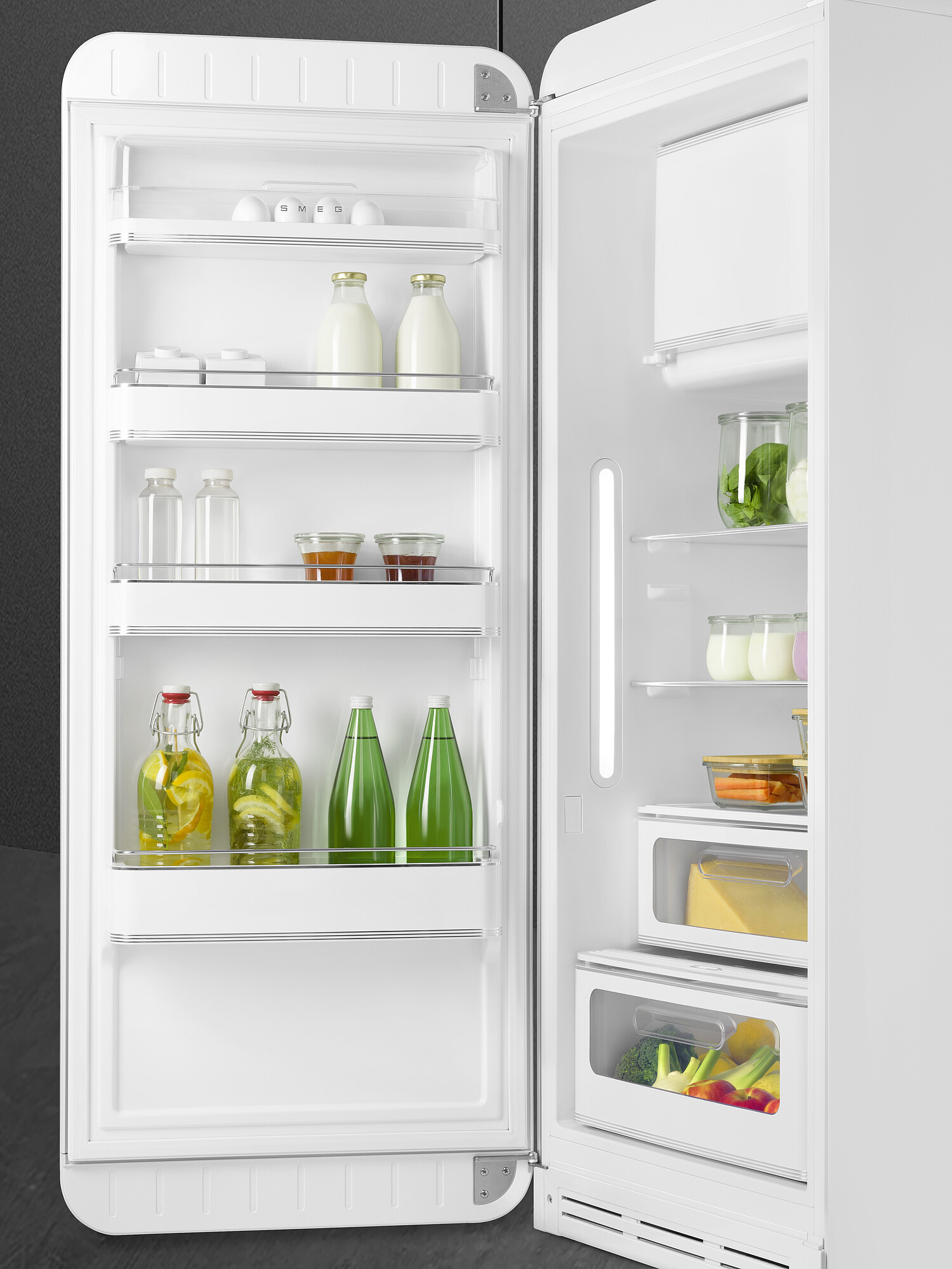 Offener weißer Kühlschrank mit Lebensmitteln. Milchflaschen, Gläser mit Getränken und Gemüse sind sichtbar.