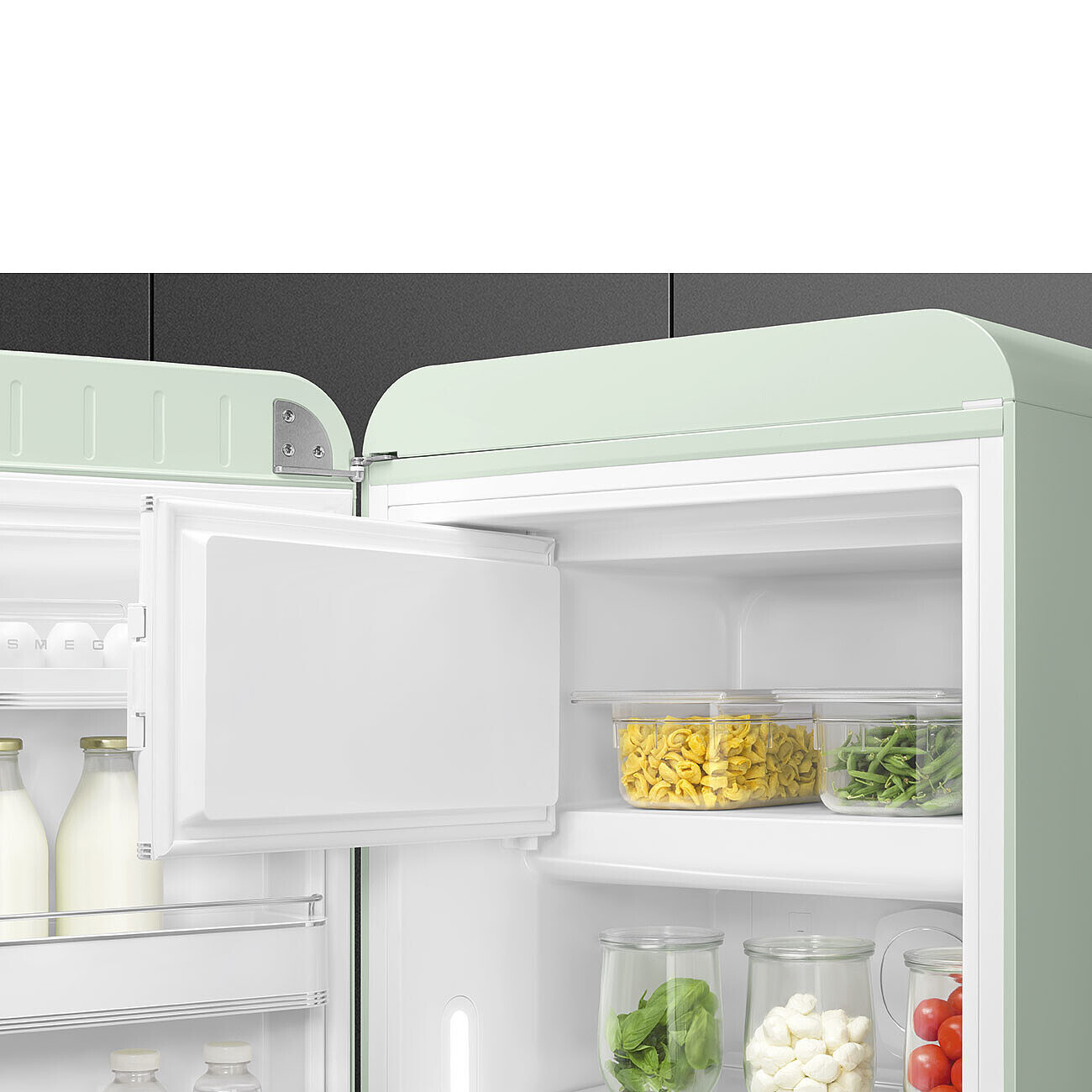 Offener mintgrüner SMEG-Kühlschrank. Innen: Nudeln, grüne Bohnen, Basilikum, Mozzarella, Tomaten. Milchflaschen in der Tür.