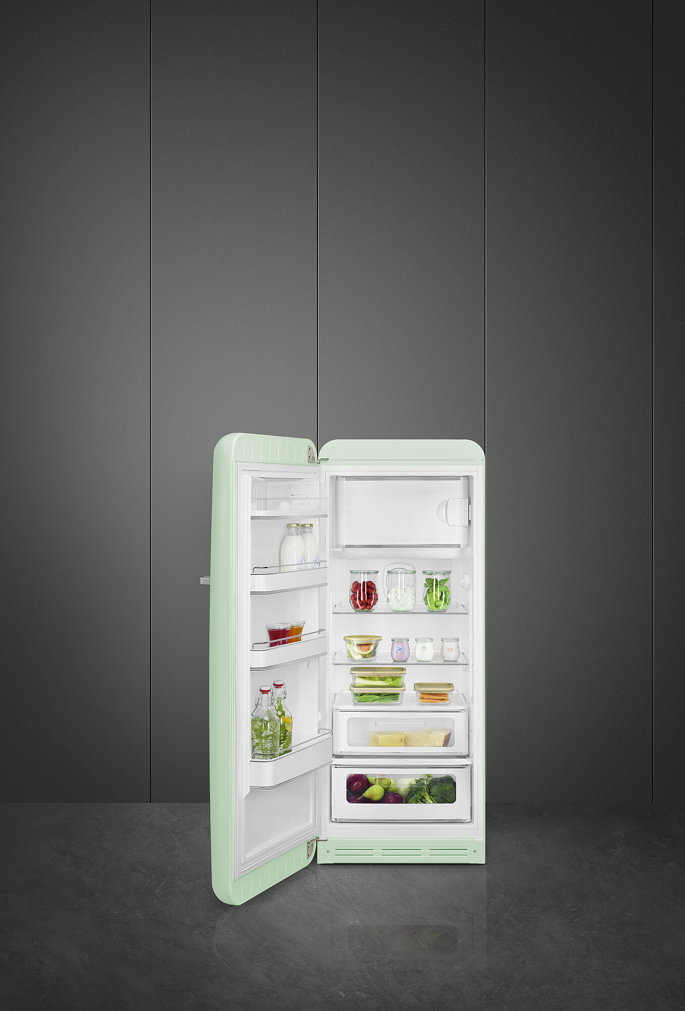Offener mintgrüner Kühlschrank. Im Inneren befinden sich Gläser, Behälter und Produkte. Grauer Wandhintergrund und Boden.