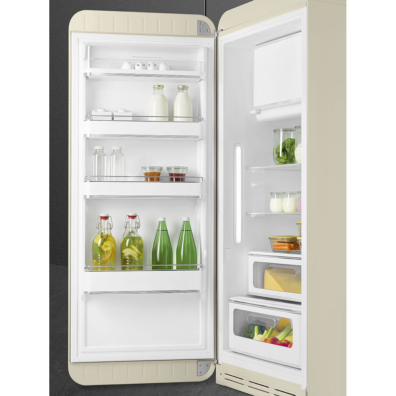 Geöffnete cremefarbene Retro-Kühlschrank, gefüllt mit Milch, Gläsern, Wasser- und Saftflaschen, Gemüse und Behältern.