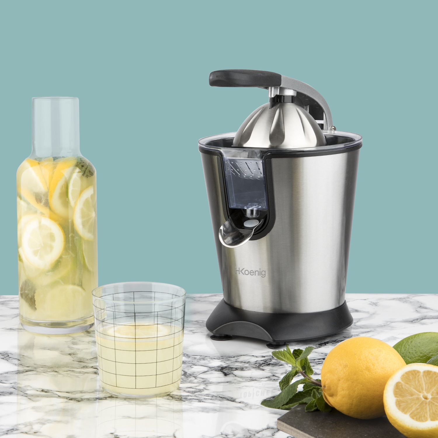 Uno spremiagrumi, un bicchiere con succo, una bottiglia con limoni e alcuni limoni e lime su un tavolo di marmo.