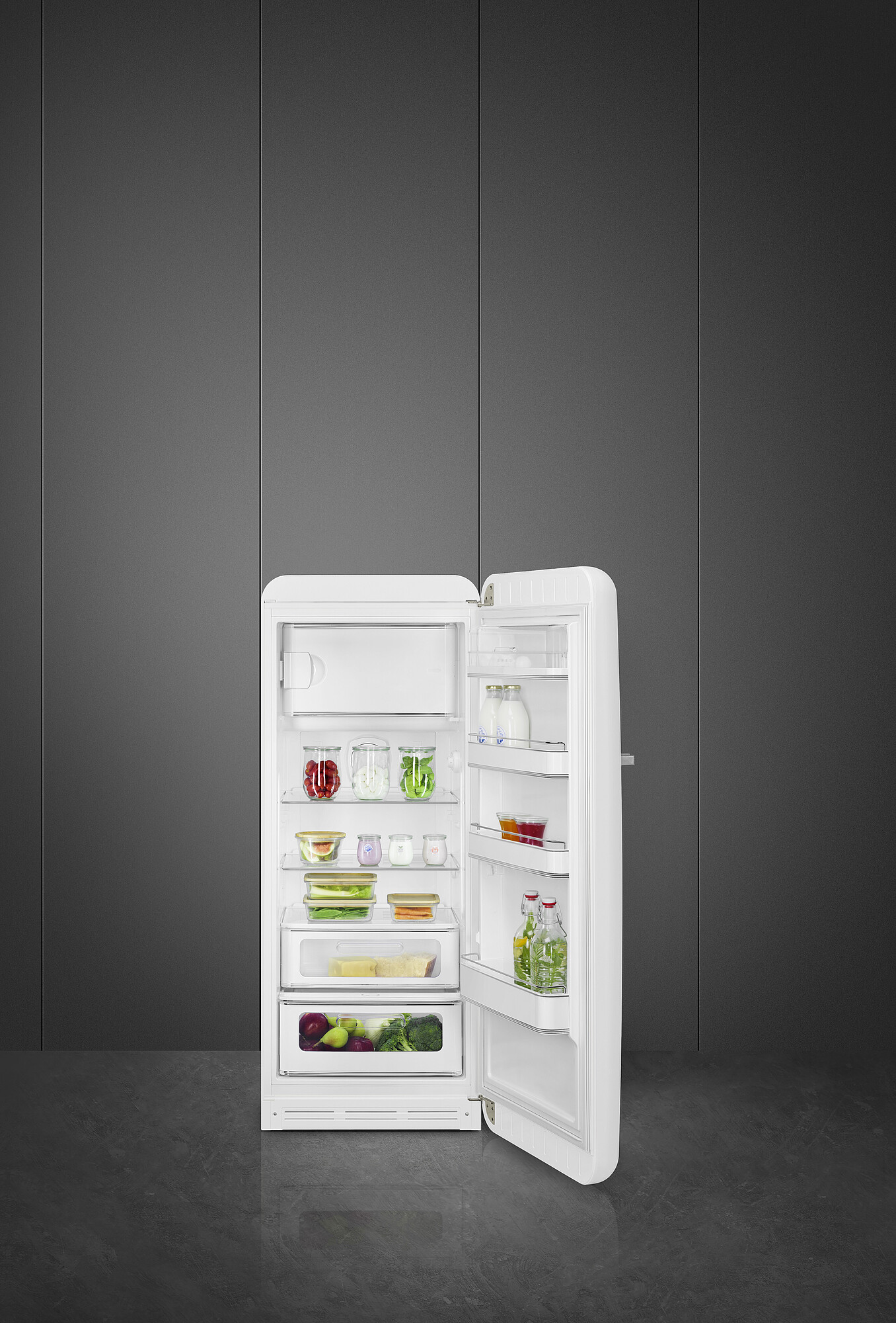 Ein weißer Retro-Kühlschrank ist geöffnet und zeigt Lebensmittel wie Beeren, Gemüse und Gläser. Der Hintergrund ist eine graue Wand.
