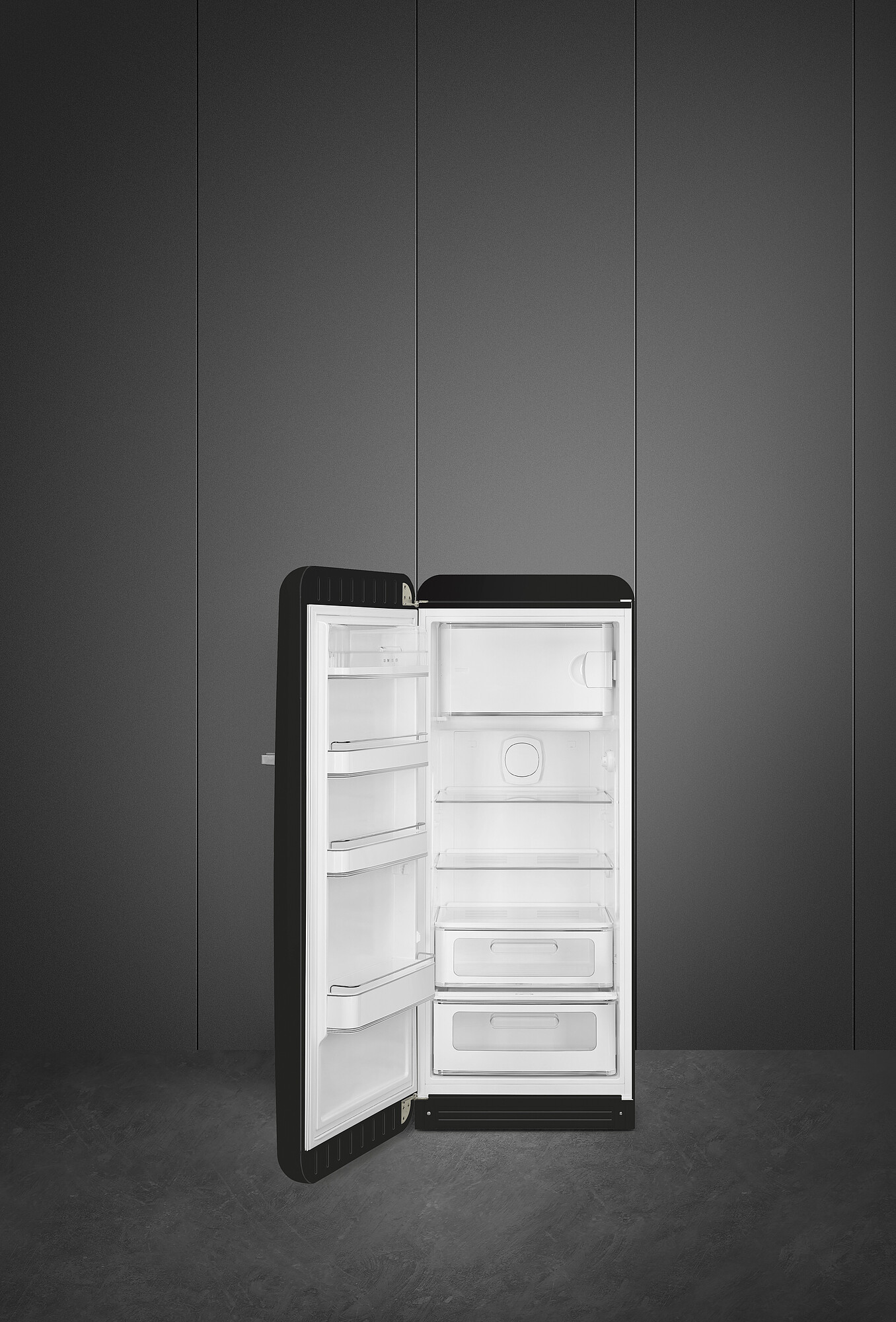 Ein schwarzer Kühlschrank mit offener Tür, der weiße Innenregale zeigt. Er steht vor einer dunkelgrauen Wand und einem dunklen Boden.