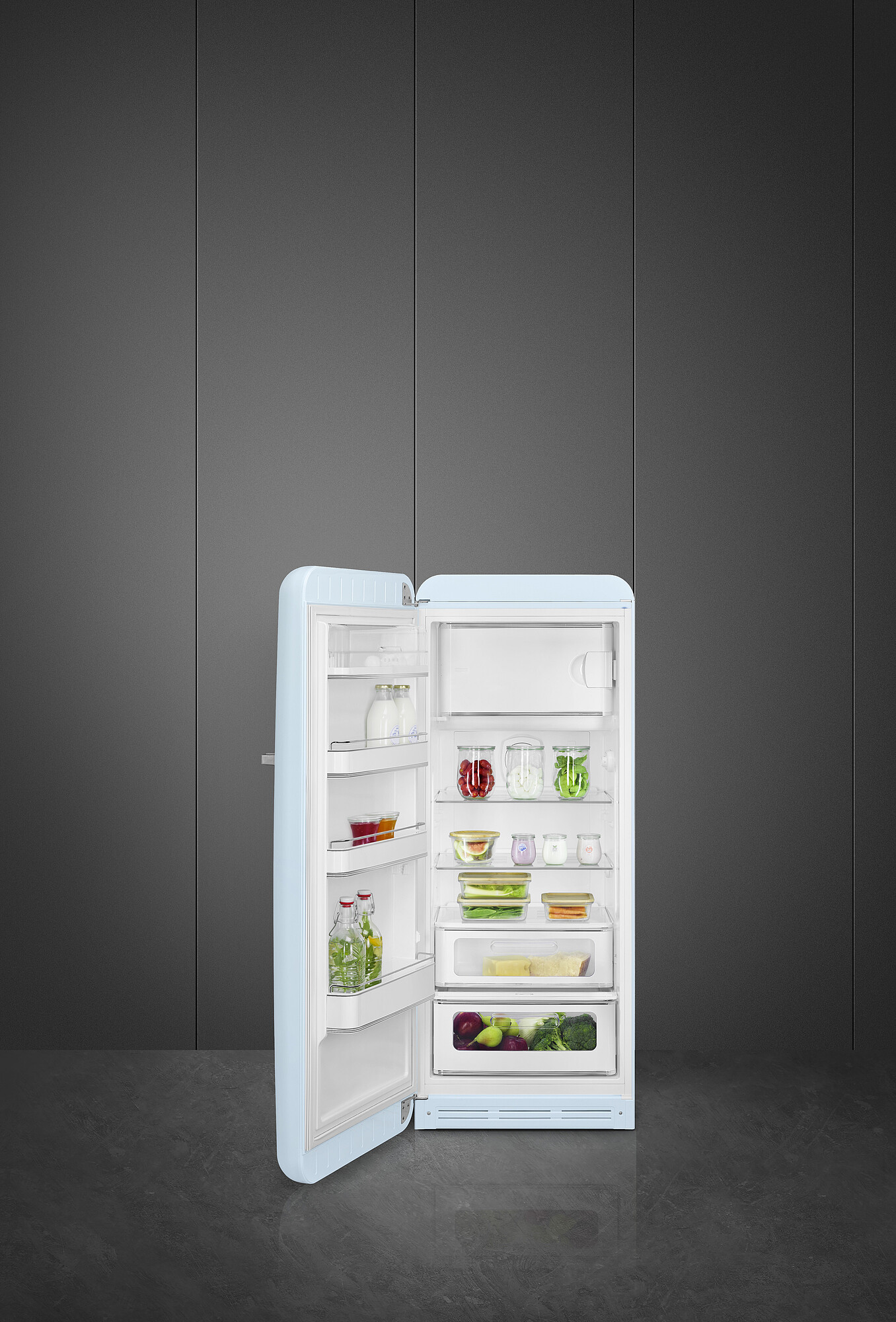Ein hellblauer Kühlschrank ist geöffnet und zeigt Regale mit Lebensmitteln vor einem dunkelgrauen Hintergrund. Der Boden ist grau.