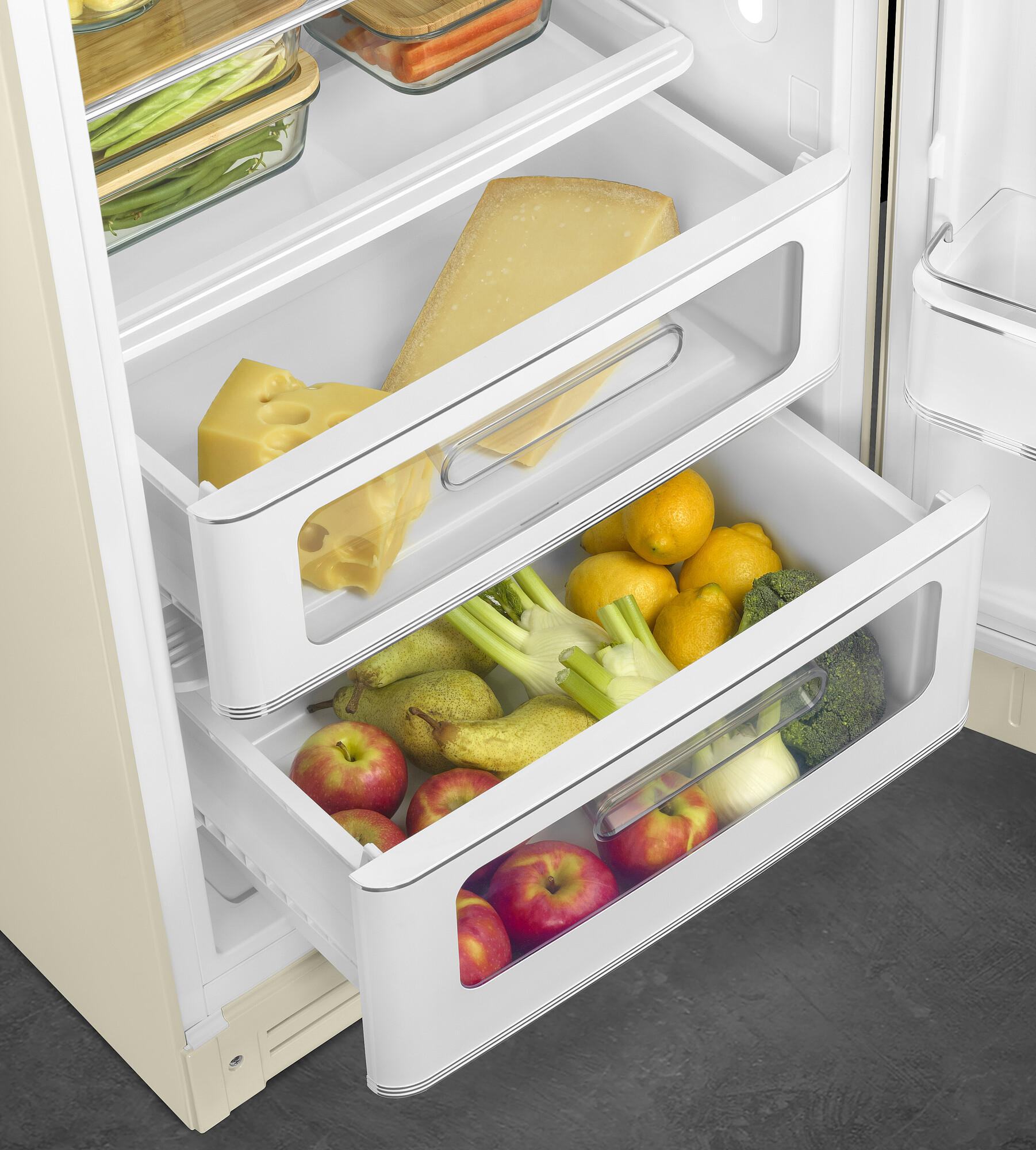 Offener Kühlschrank mit Schubladen voller Käse, Zitronen, Äpfel, Birnen, Brokkoli und Fenchel. Beigefarbener Kühlschrank mit dunklem, grauem Boden.