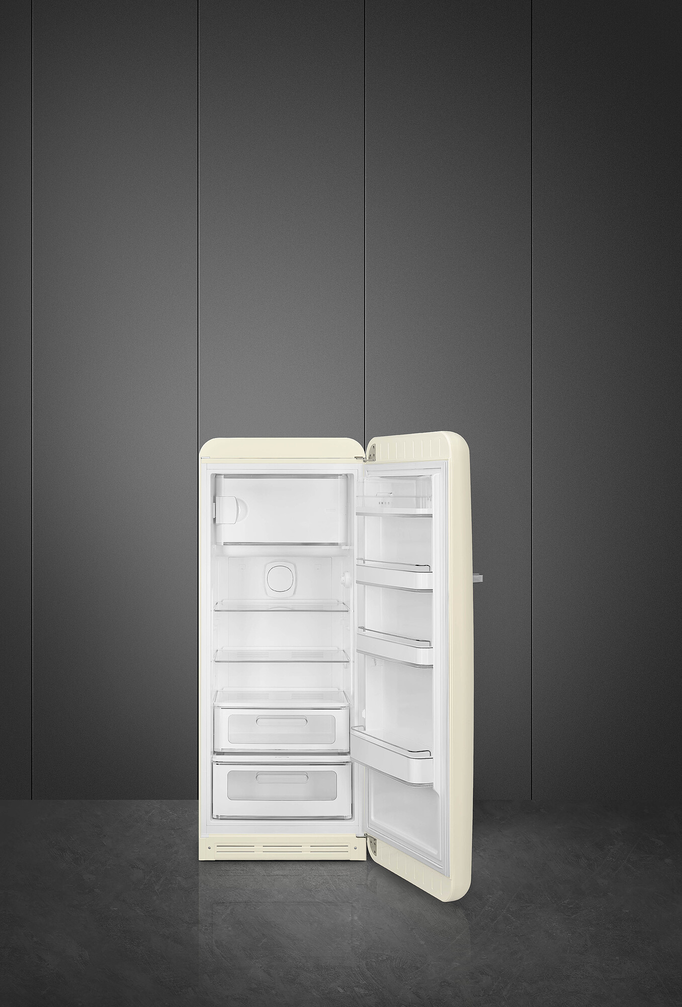 Offener cremefarbener Kühlschrank vor einer dunkelgrauen Wand. Innen sind weiße Regale und Schubladen sichtbar. Der Boden ist grau.