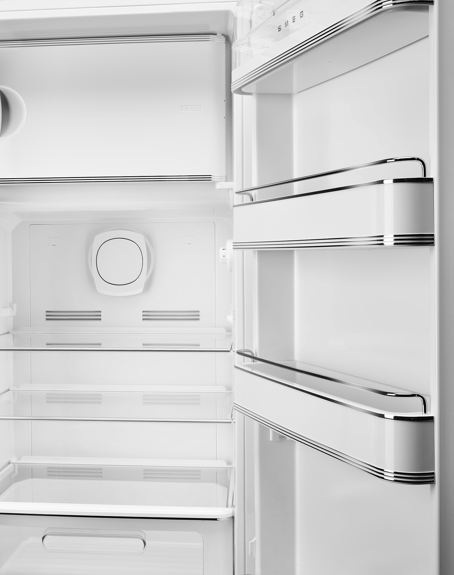 Offener weißer Kühlschrankinnenraum mit Regalen, Tür und einer kreisförmigen Komponente. SMEG-Logo sichtbar.