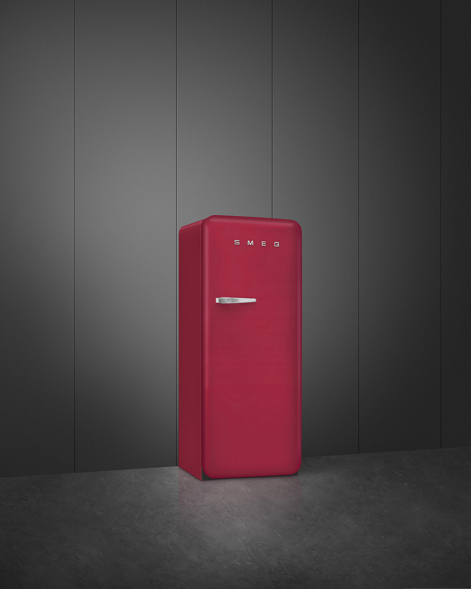 Ein roter SMEG-Kühlschrank steht vor einer dunkelgrauen Wand und einem grauen Boden. Der Kühlschrank hat einen silbernen Griff.