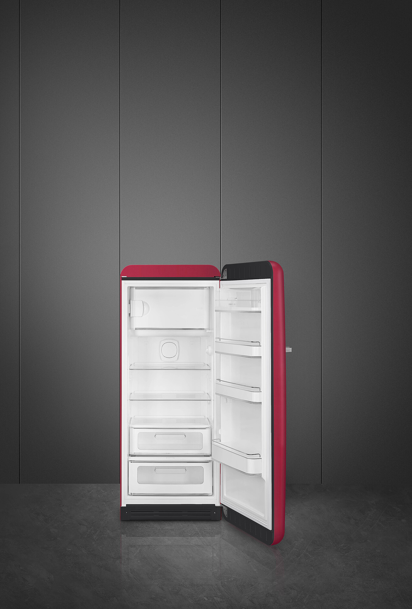Ein roter Kühlschrank mit offener Tür steht auf dunklem Boden. Der Hintergrund ist eine graue Wand.
