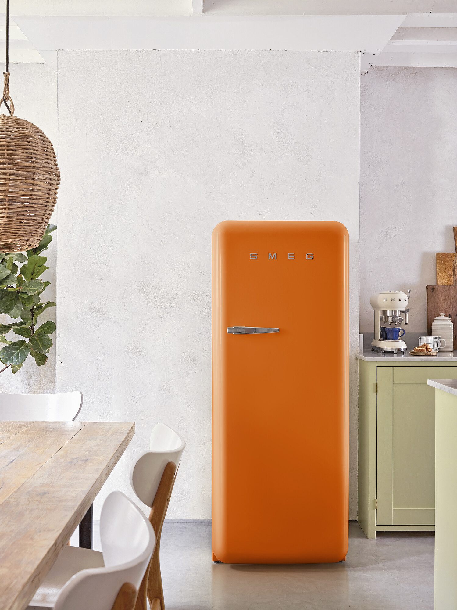Ein orangefarbener Smeg-Kühlschrank steht in einer Küche. Ein Holztisch und weiße Stühle sind im Vordergrund.