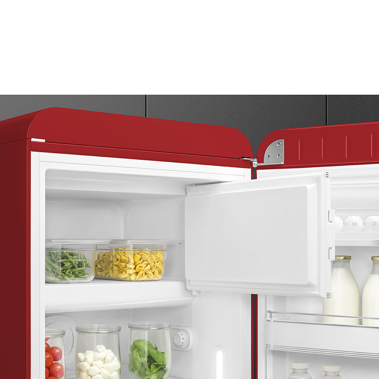 Offener roter Kühlschrank. Im Inneren befinden sich Gemüse, Nudeln, Milchflaschen und Gläser. Die Tür ist offen und zeigt das Innere.