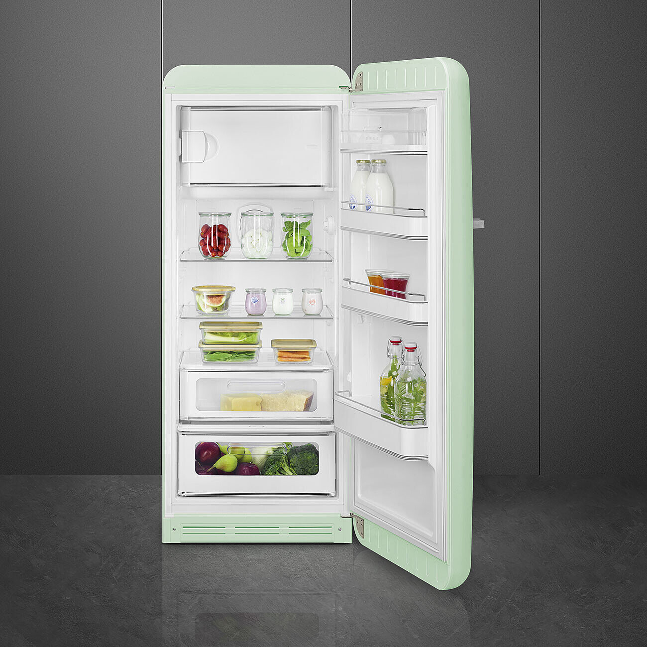 Offener mintgrüner Kühlschrank mit Lebensmitteln gefüllt. Gläser mit Obst und Gemüse, Milchflaschen und andere Behälter sind sichtbar.