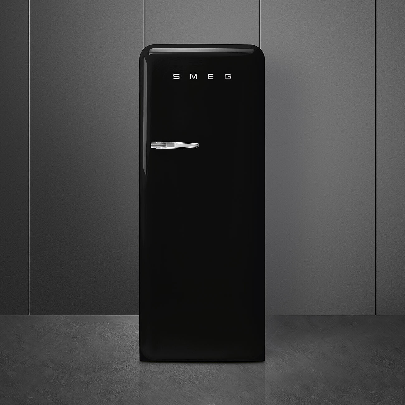 Ein schwarzer SMEG-Kühlschrank steht vor einer grauen Wand. Der Kühlschrank hat einen silbernen Griff und den Markennamen oben.