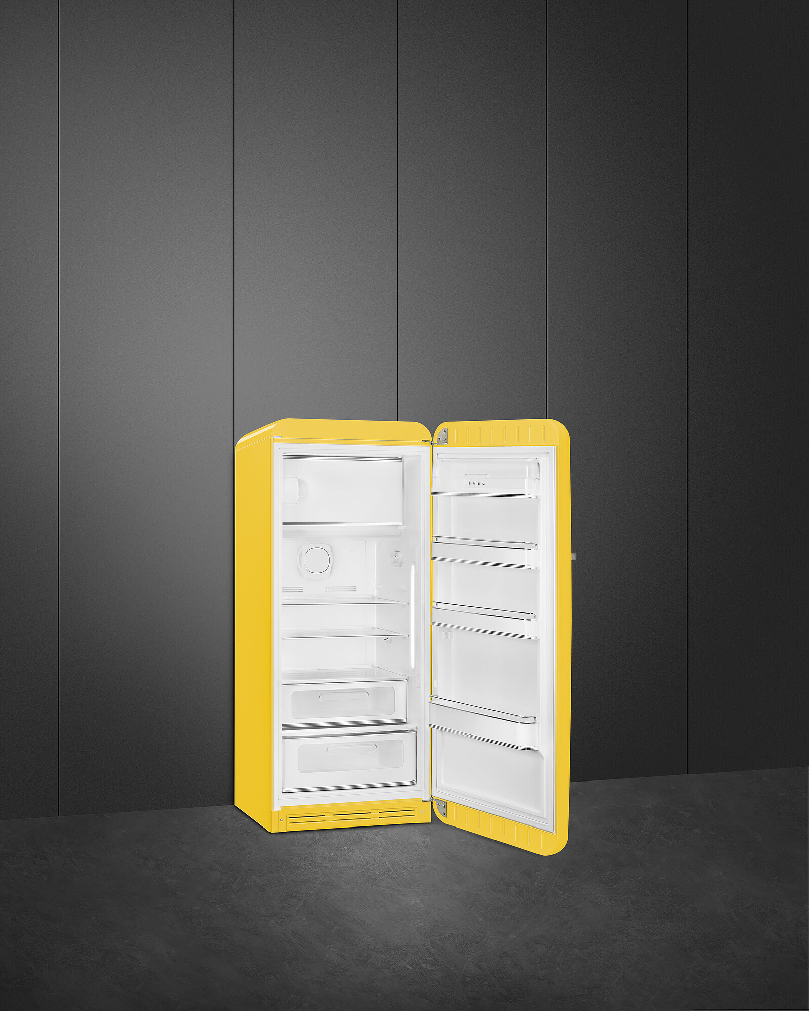 Ein gelber Kühlschrank mit offener Tür steht vor einer dunkelgrauen Wand. Die Innenseite ist weiß.