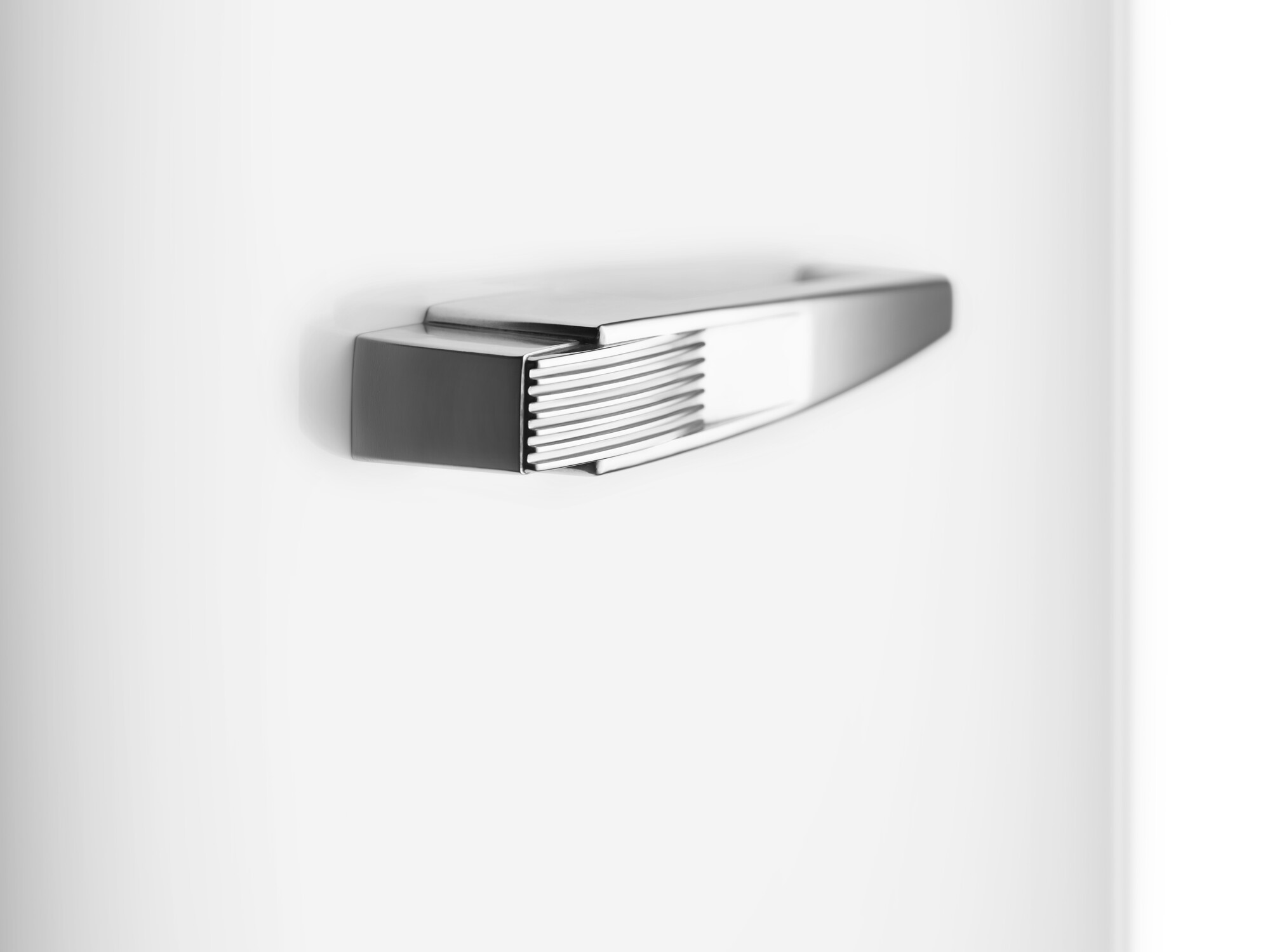 Ein metallischer Gegenstand ist auf einer weißen Oberfläche montiert. Er ist rechteckig mit einem gerippten Abschnitt und glatter, reflektierender Oberfläche.