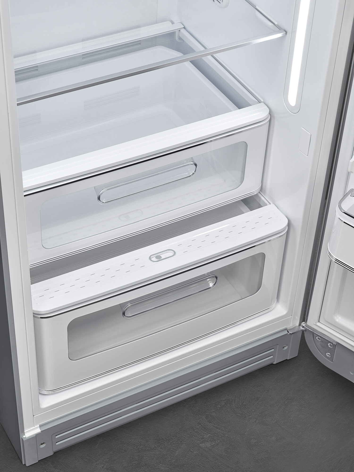 Offener weißer Kühlschrank mit zwei transparenten Schubladen. Metallgriffe und Regale. Grauer Boden sichtbar.
