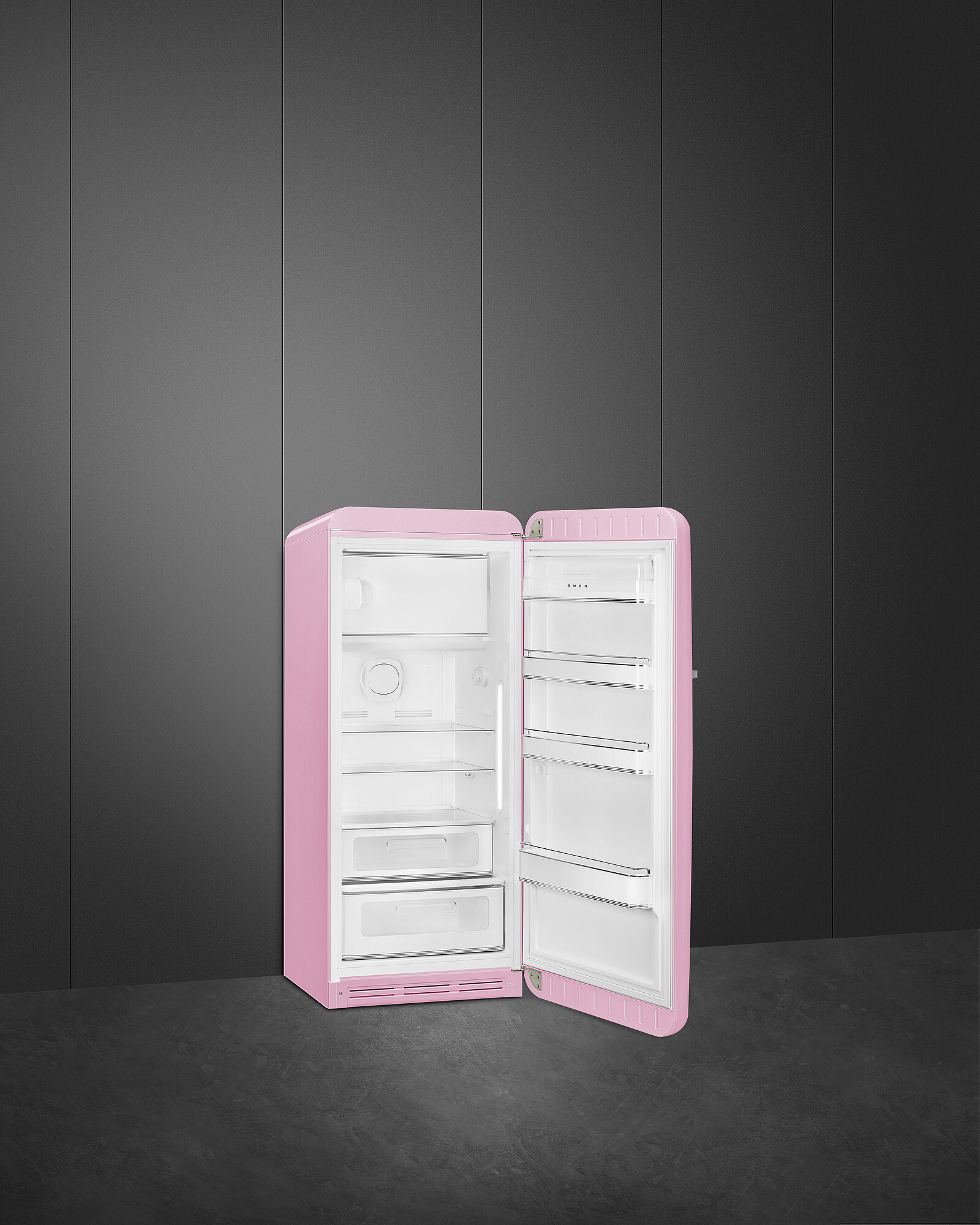 Rosa Retro-Kühlschrank mit geöffneter Tür, vor dunkler grauer Wand und Boden. Innenraum weiß.