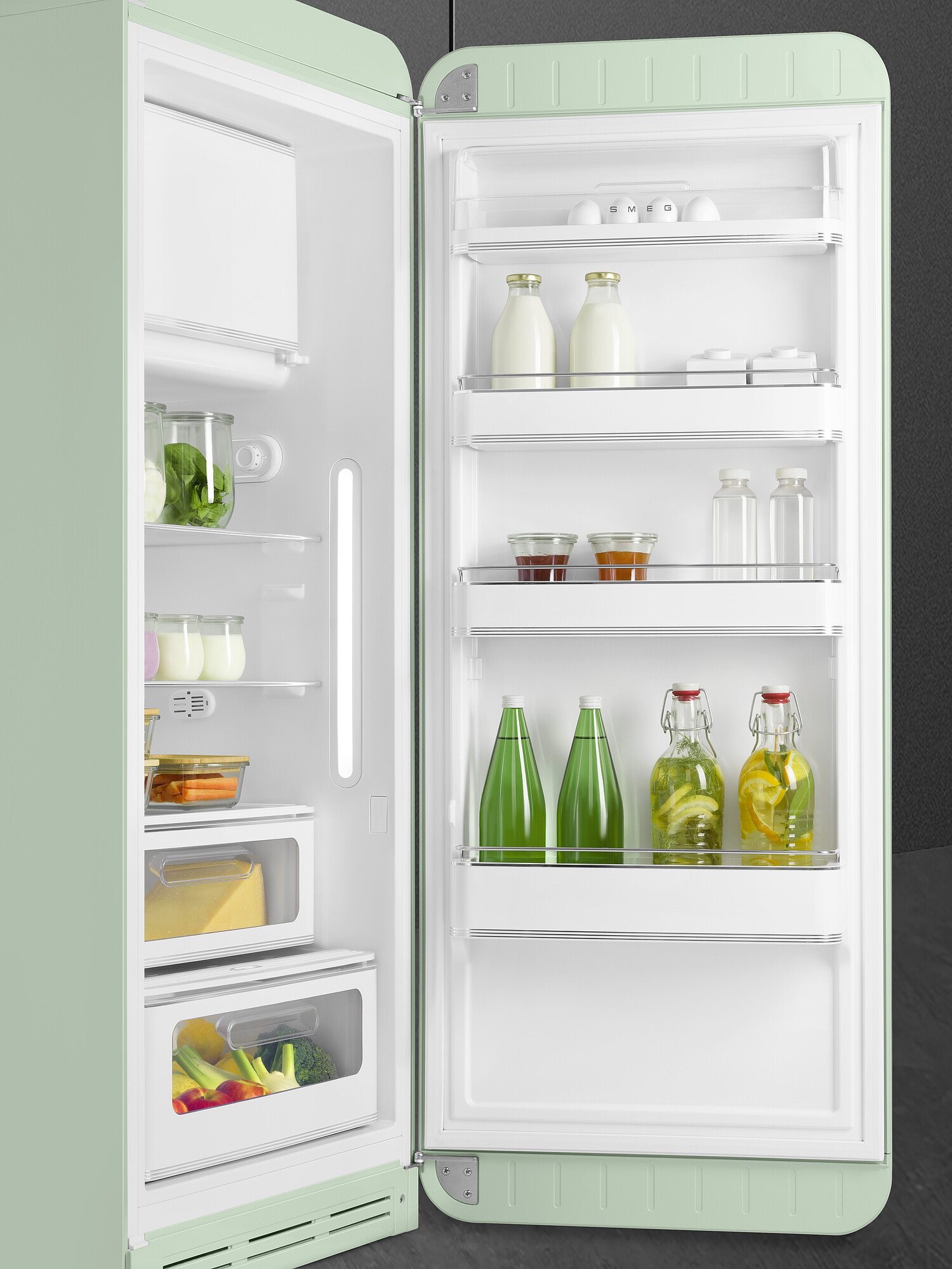 Offener mintfarbener Kühlschrank voller Lebensmittel: Milch, Eier, Gemüse, Getränke. Innenbeleuchtung ist an. Der Hintergrund ist dunkel.