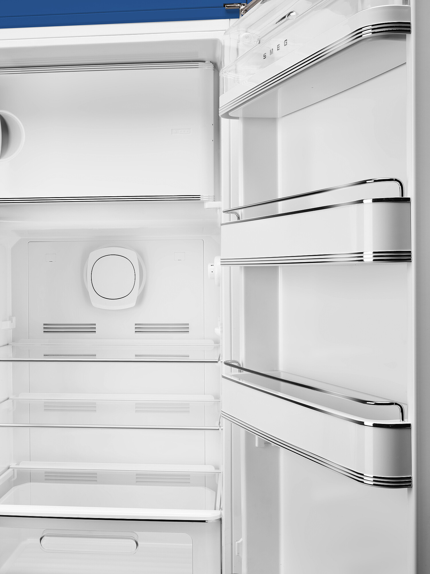 Innenraum eines offenen weißen Kühlschranks. Regale, Schubladen und ein kreisförmiges Element sind sichtbar. Die Marke SMEG steht oben.