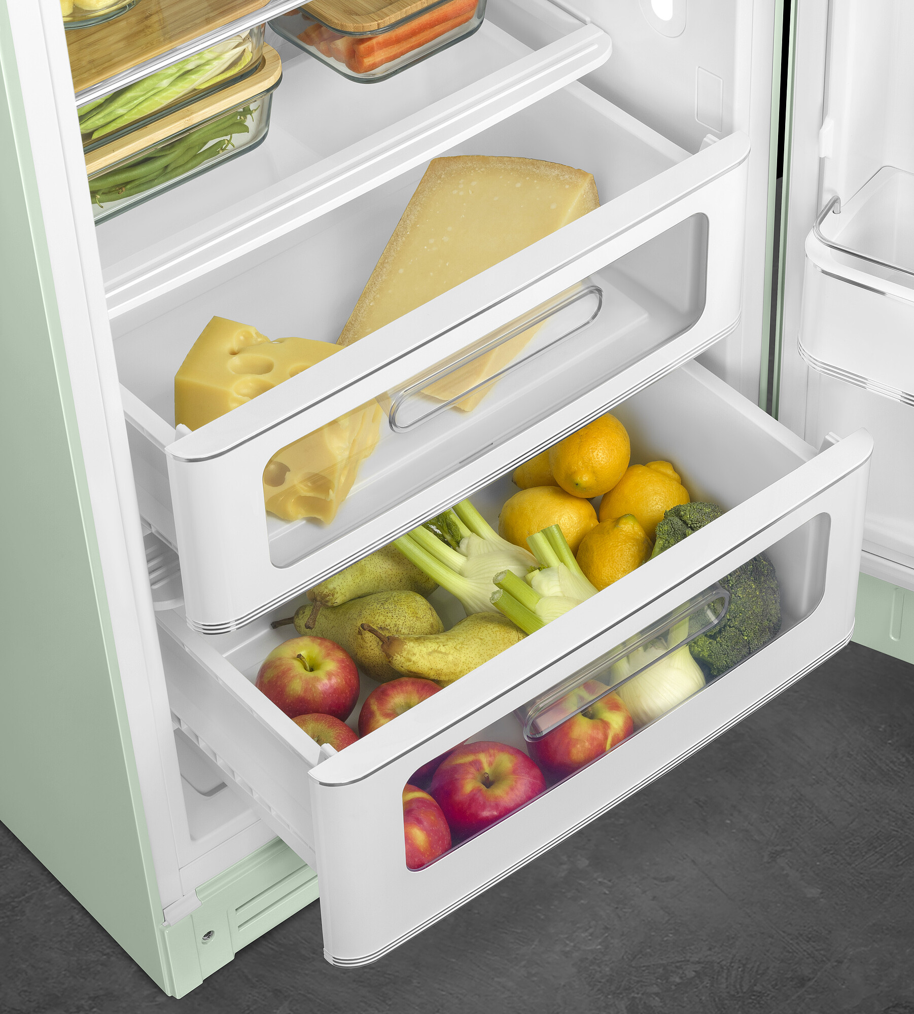 Offener Kühlschrank mit Käse, Zitronen, Äpfeln, Birnen, Fenchel und Brokkoli in Schubladen. Grüne Tür, weiße Innenausstattung.