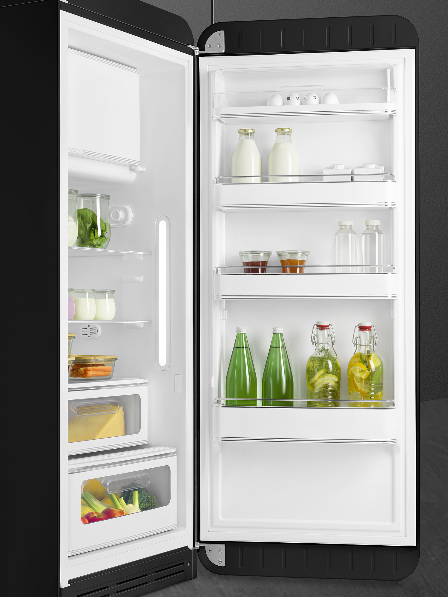 Offener schwarzer Kühlschrank. Im Inneren befinden sich verschiedene Lebensmittel wie Gemüse, Milchflaschen, Gläser mit Marmelade und Flaschen mit Wasser und Zitrone.