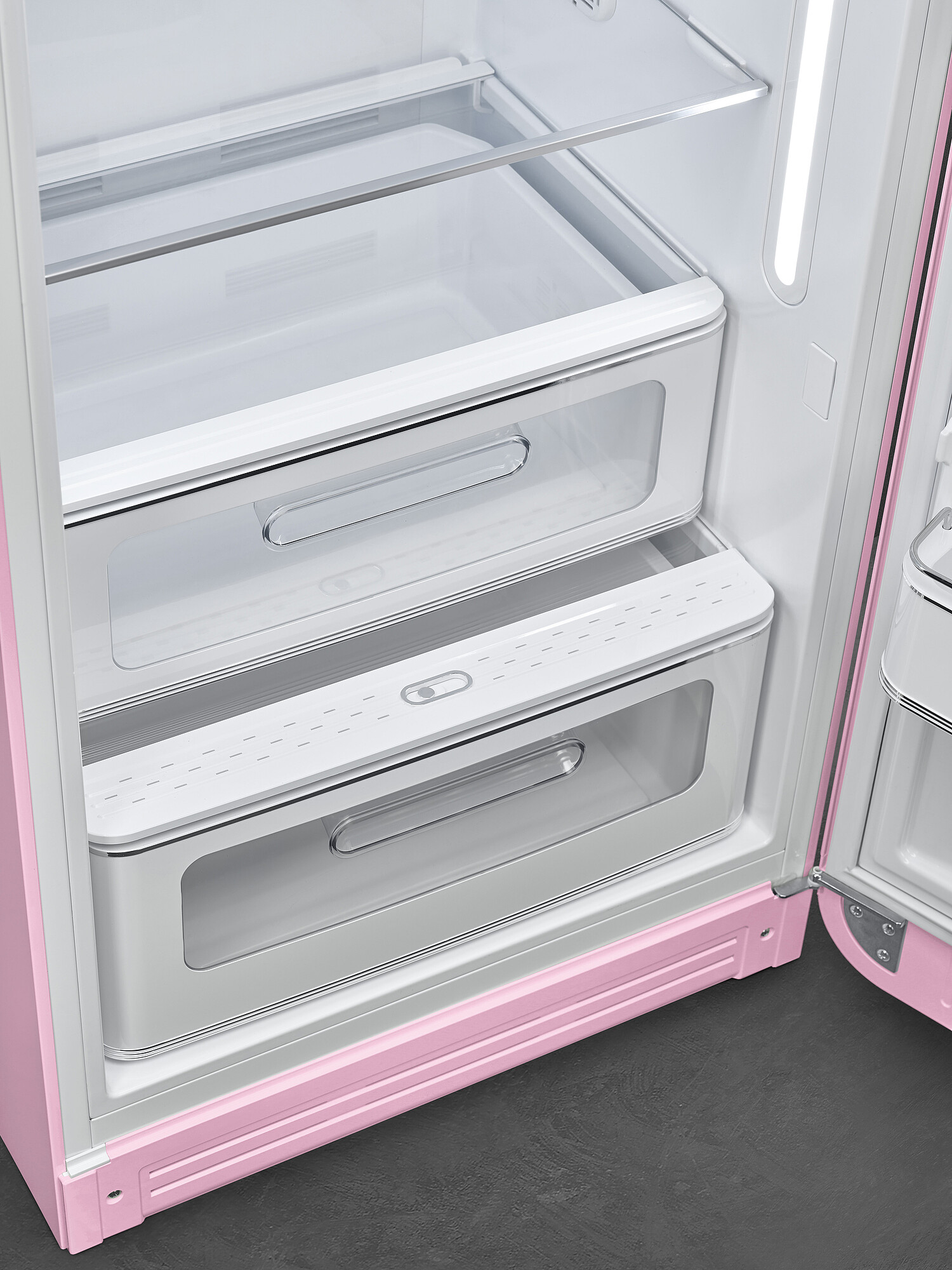 Offener rosa Kühlschrank. Sichtbar sind Schubladen, Regale und ein Licht. Der Kühlschrank ist weiß mit rosa Akzenten und grauem Boden.
