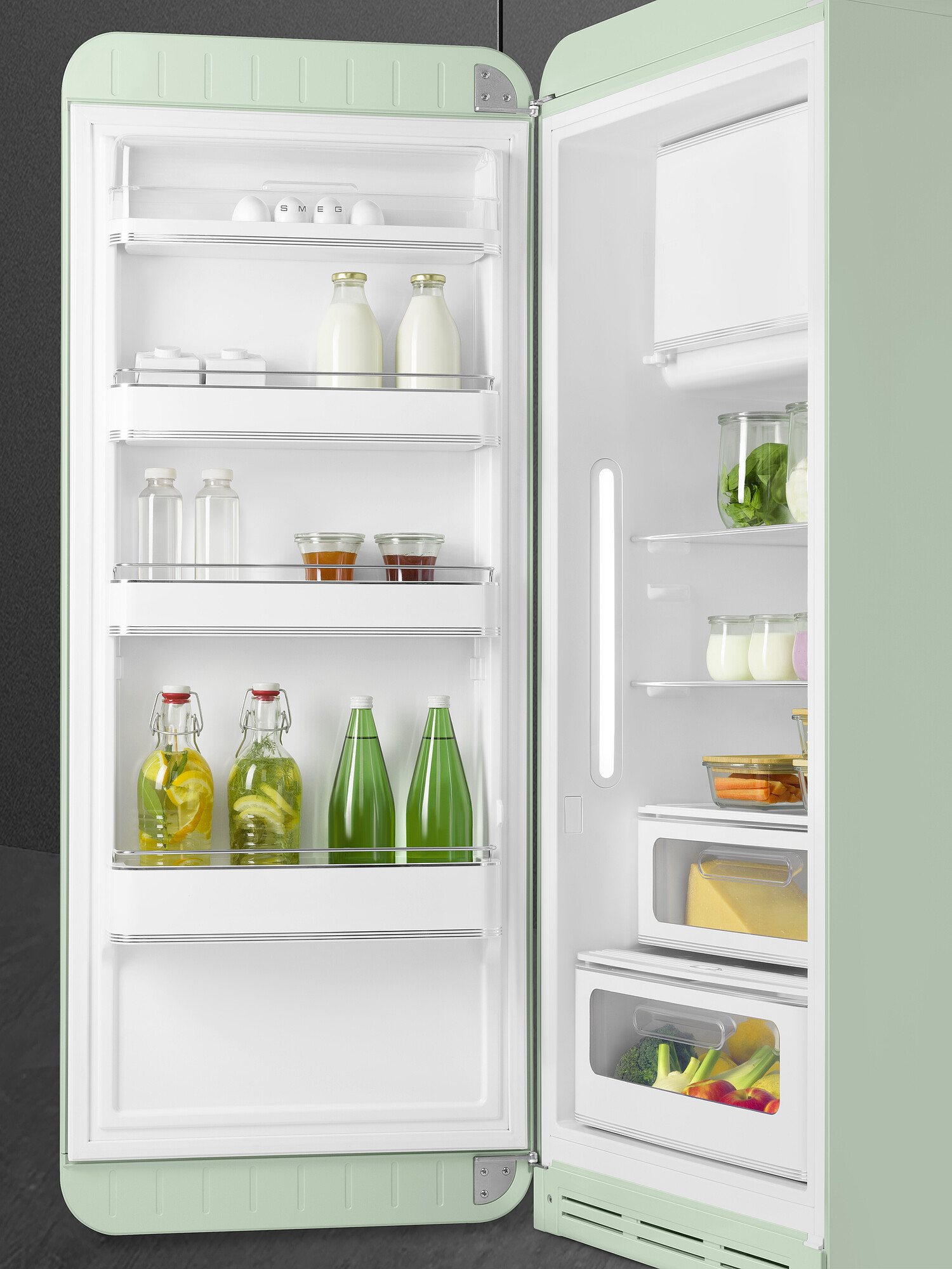 Offener mintgrüner Retro-Kühlschrank. Im Inneren befinden sich Eier, Milchflaschen, Wasserflaschen, Gläser mit Lebensmitteln und Gemüse.