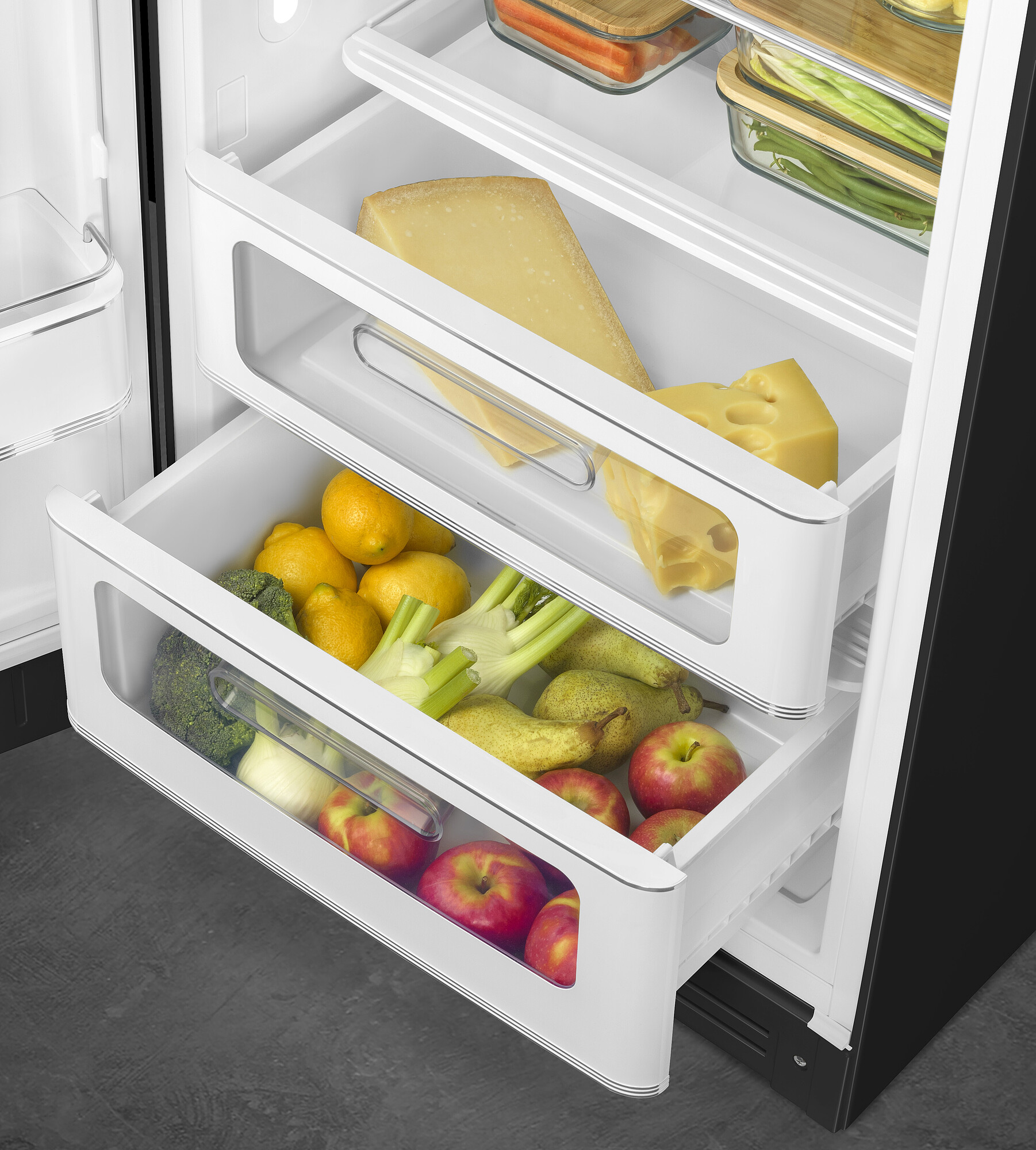 Offener Kühlschrank mit Schubladen. Käse, Zitronen, Äpfel, Birnen, Brokkoli und Fenchel sind sichtbar. Glasbehälter mit Karotten und Bohnen.