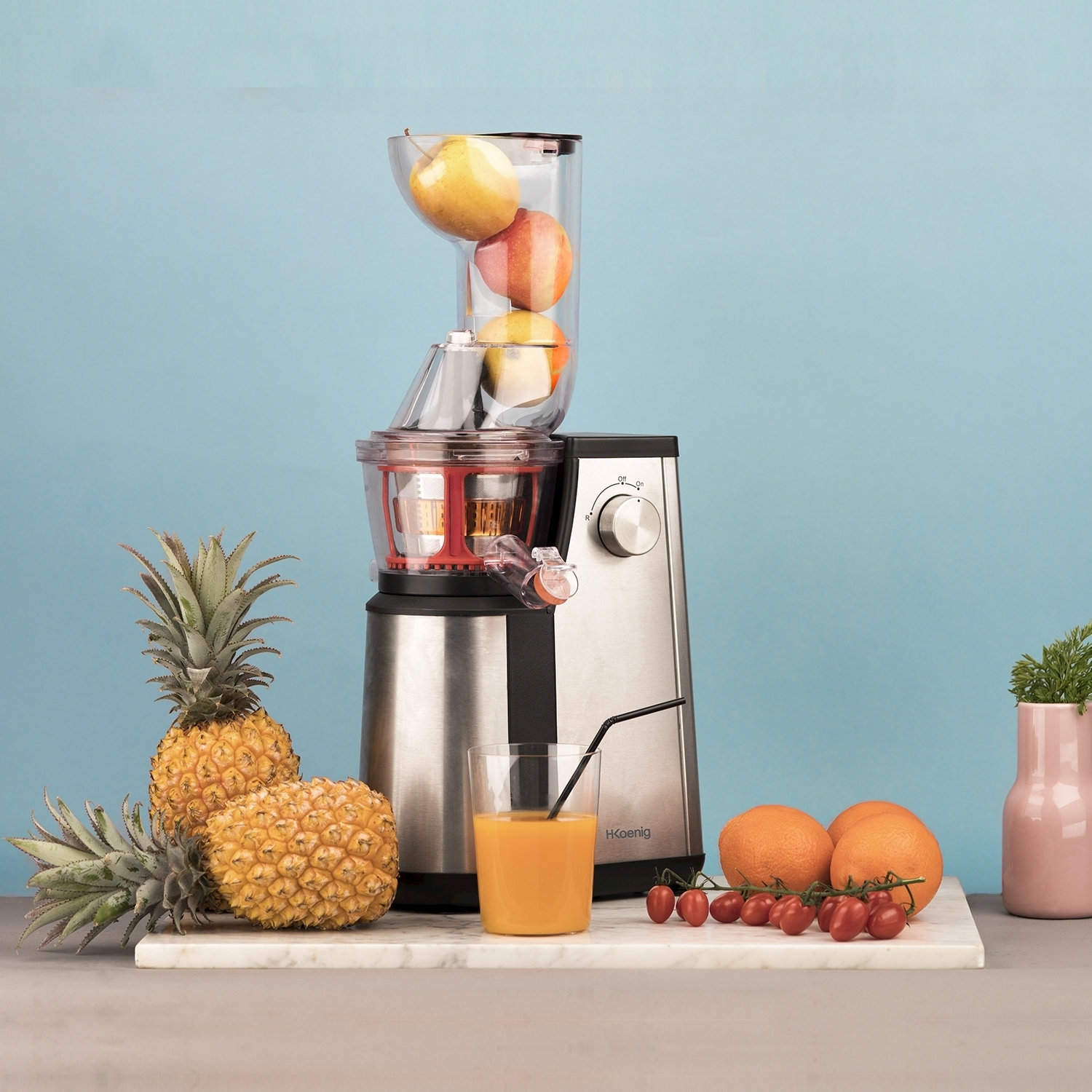 Centrifuga con frutta. Ananas, arance, pomodori e un bicchiere di succo su marmo. Sfondo blu.