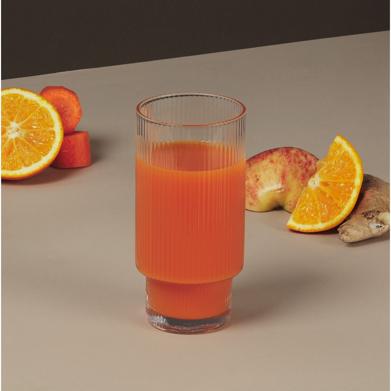 Un bicchiere di succo d'arancia con frutta e verdura intorno. Include arance, pesche, carote e zenzero.
