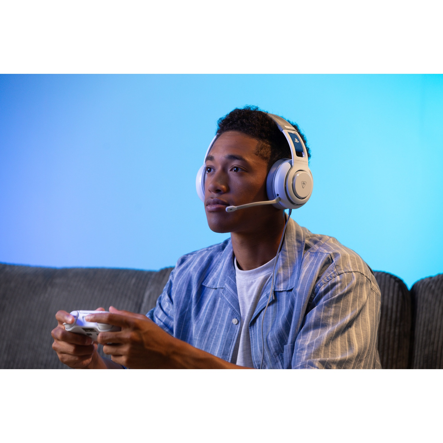 A young man wearing a headset plays a game, holding a controller. He's on a couch, with a blue gradient background.